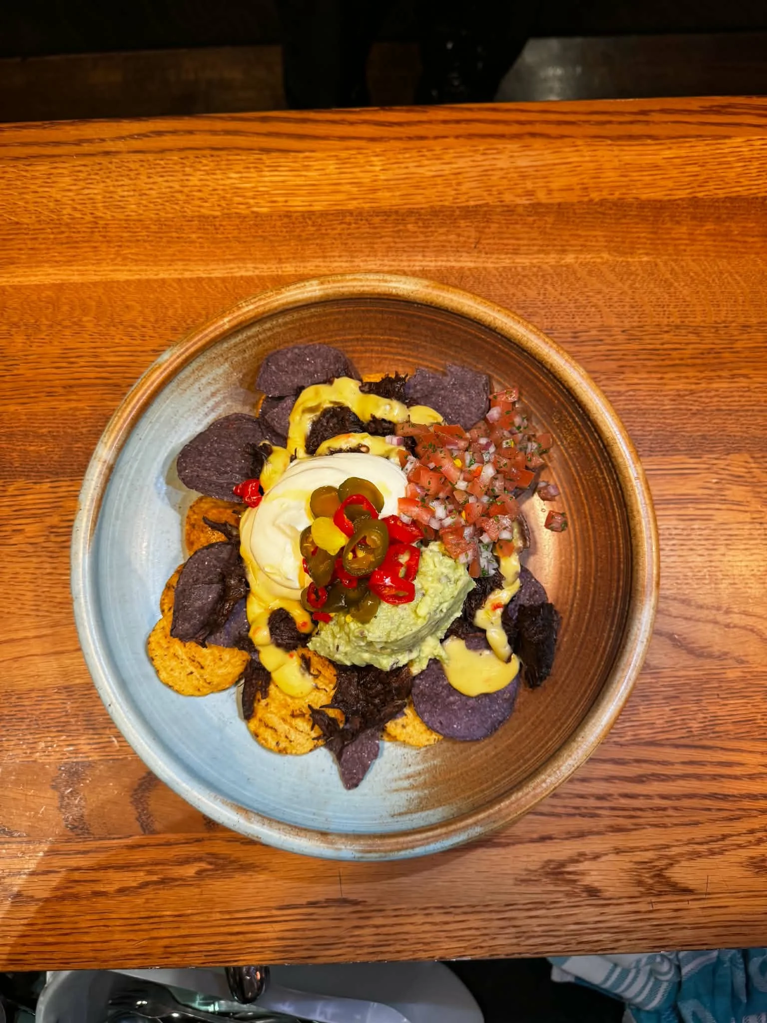 A plate of Mexican food with chips, guacamole, sour cream, pickled jalapenos, diced tomatoes, and various salsas on a wooden table.