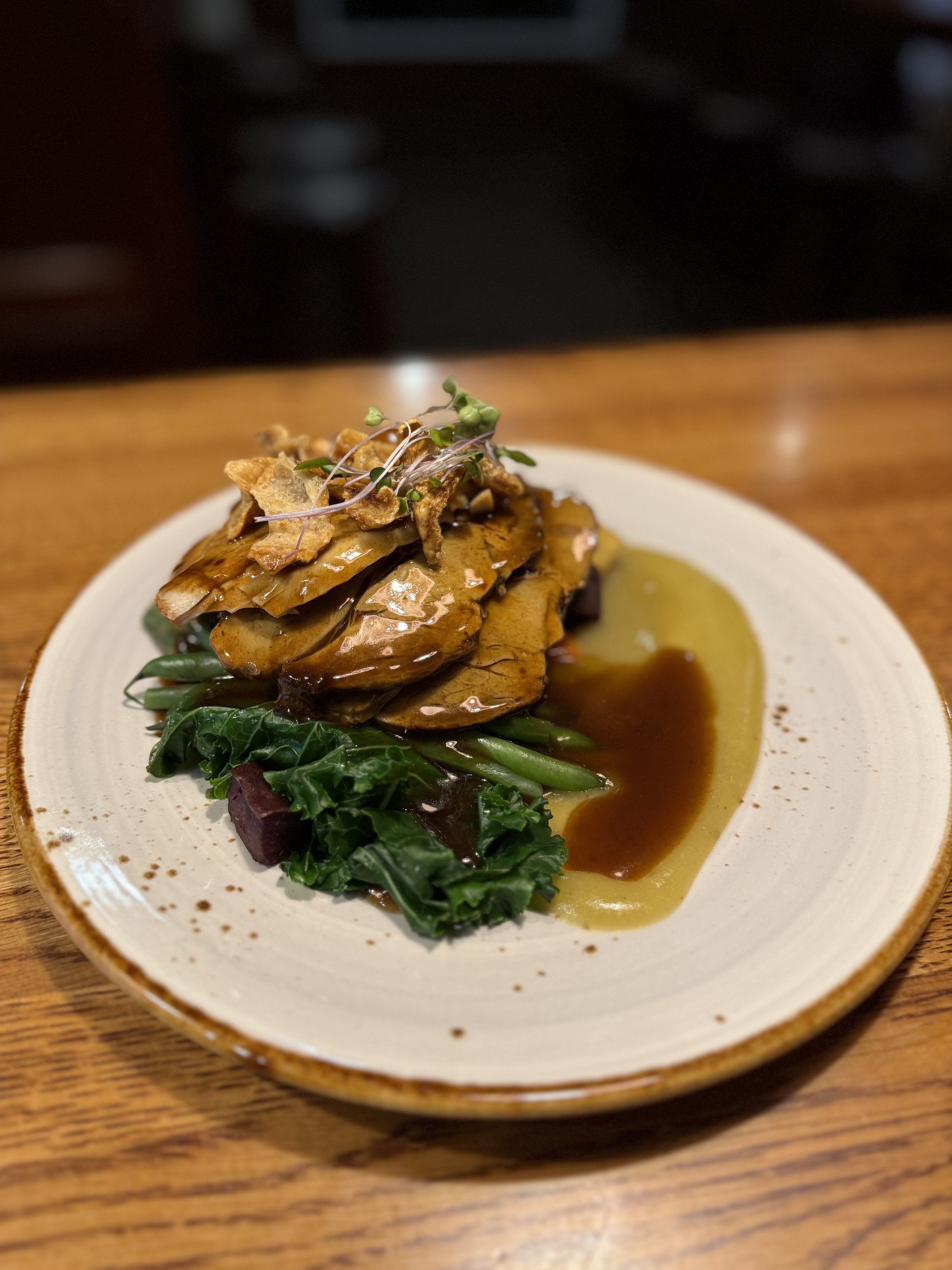 A plate with glazed roasted eggplant slices topped with microgreens, served with greens and a brown sauce.