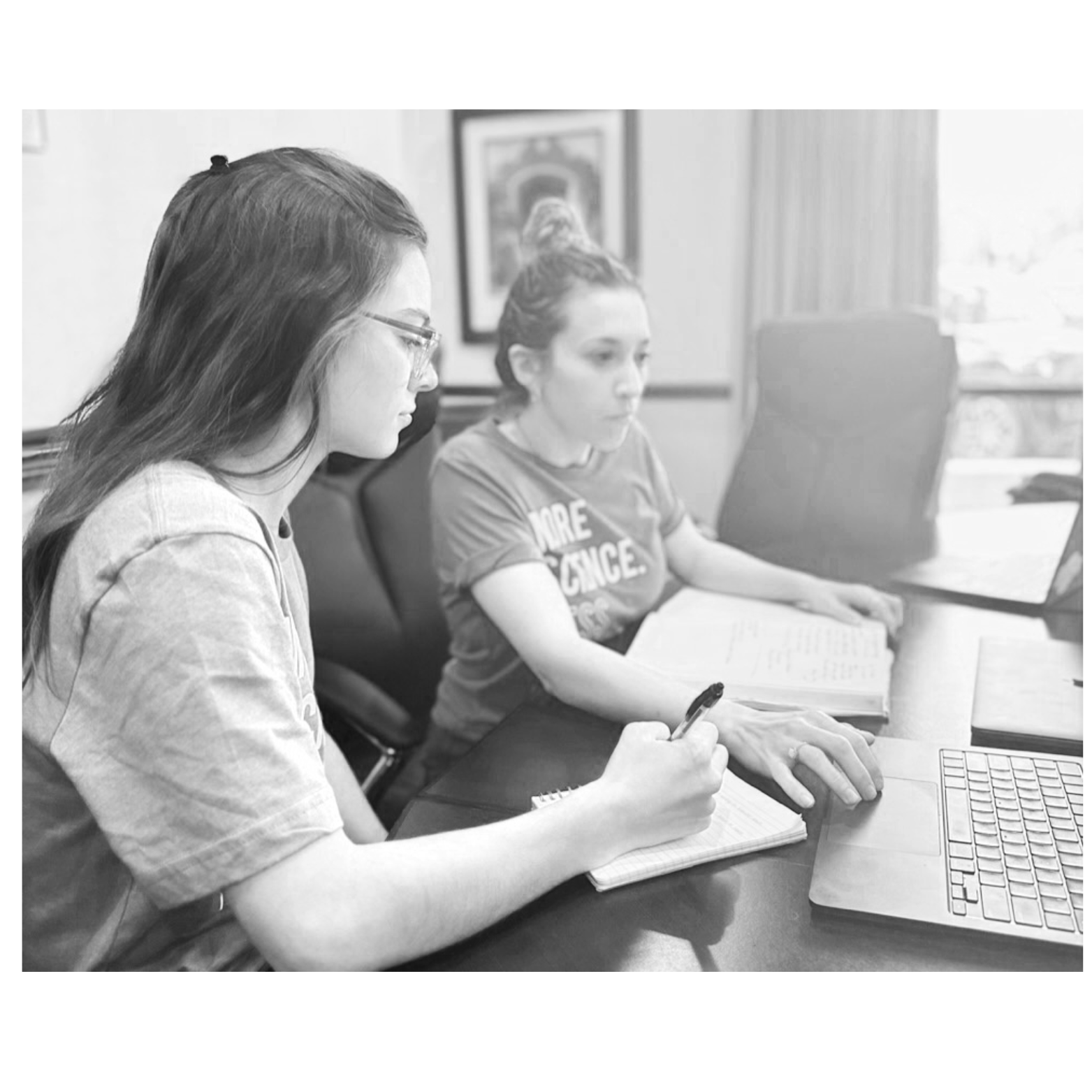Two people are working at a desk with a laptop and notebooks.