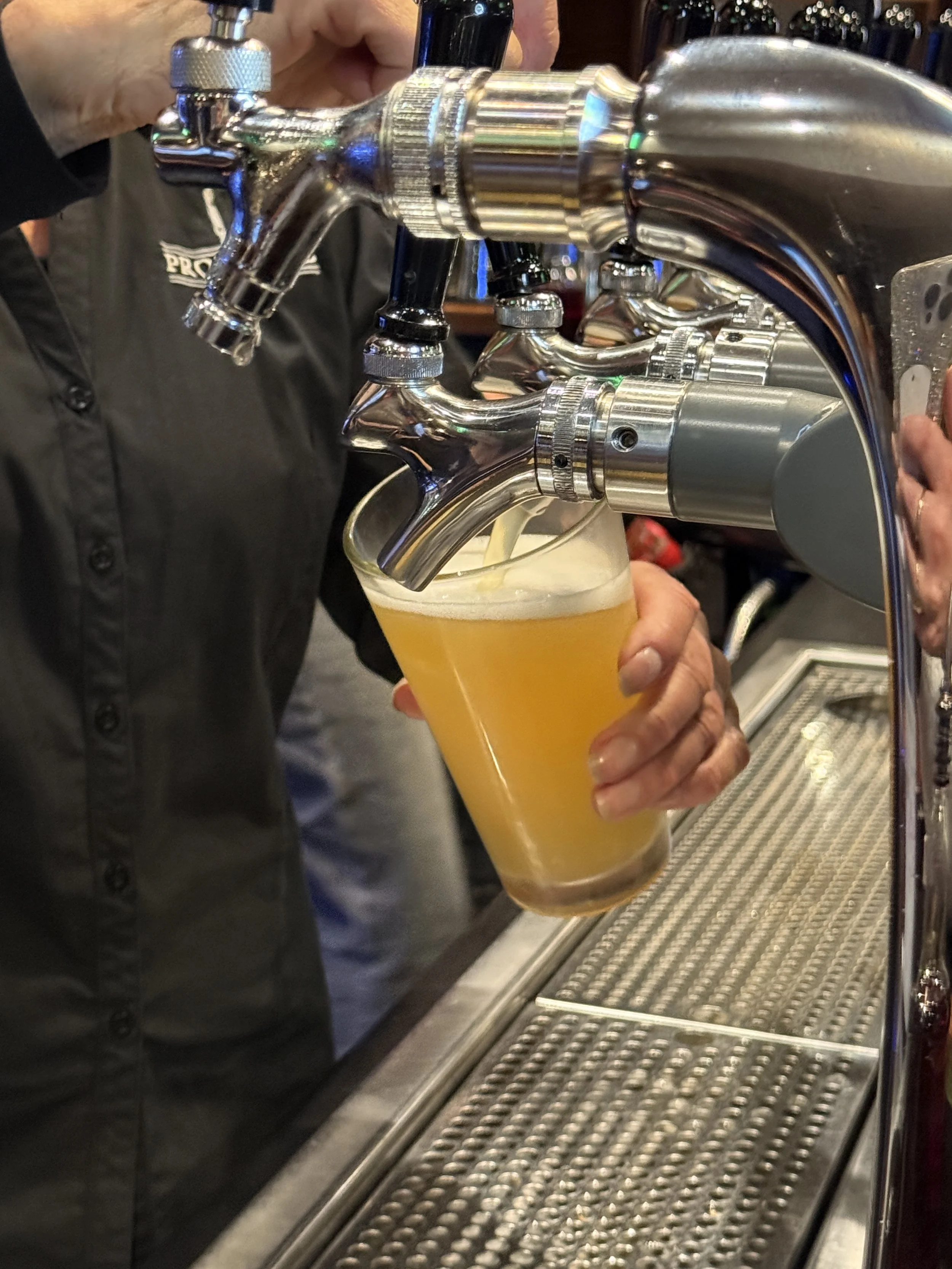 A person pouring a hazy, yellowish beer from a tap into a glass at a bar.