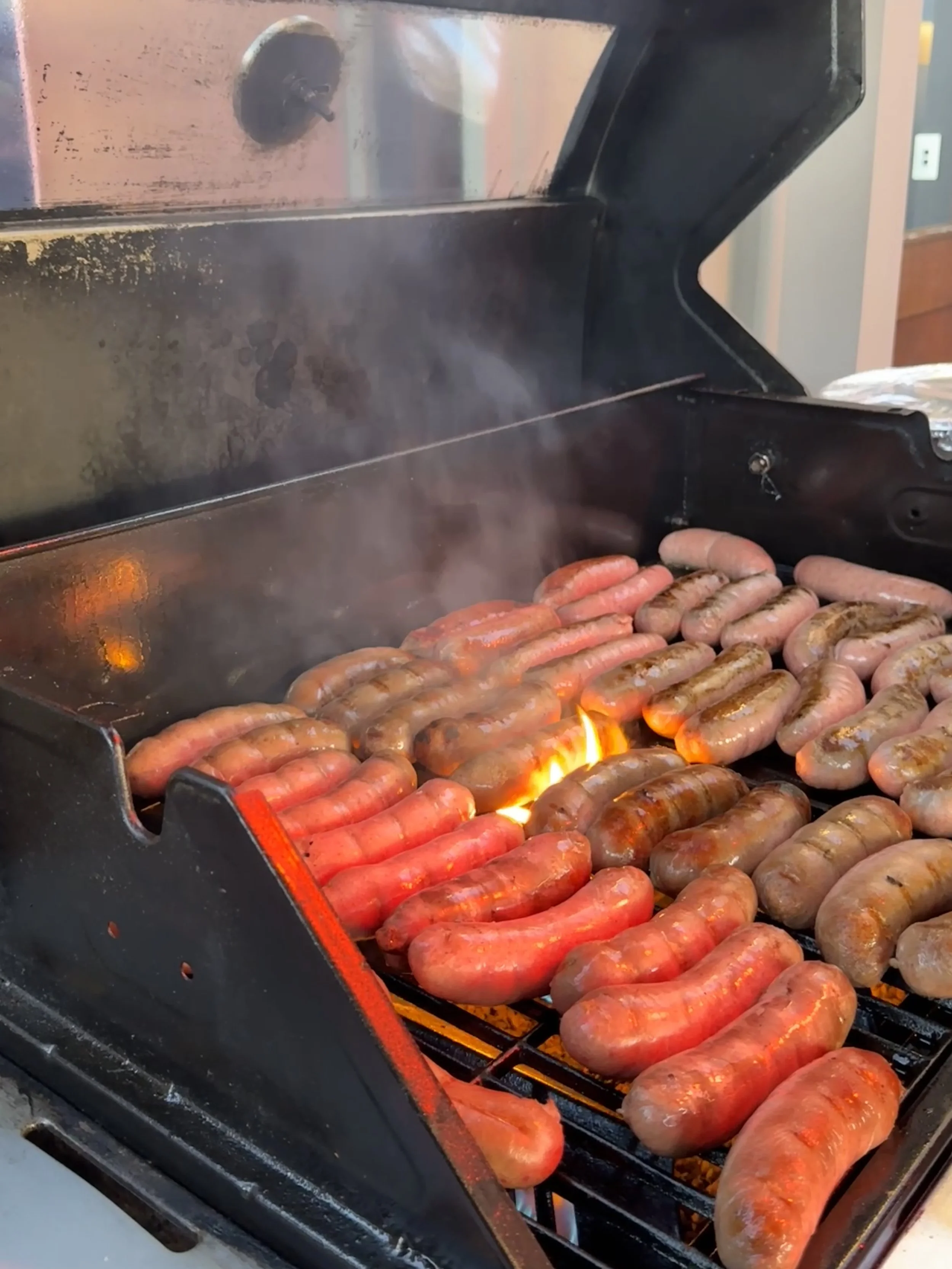 Hot dogs and sausages grilling on an outdoor barbecue grill.