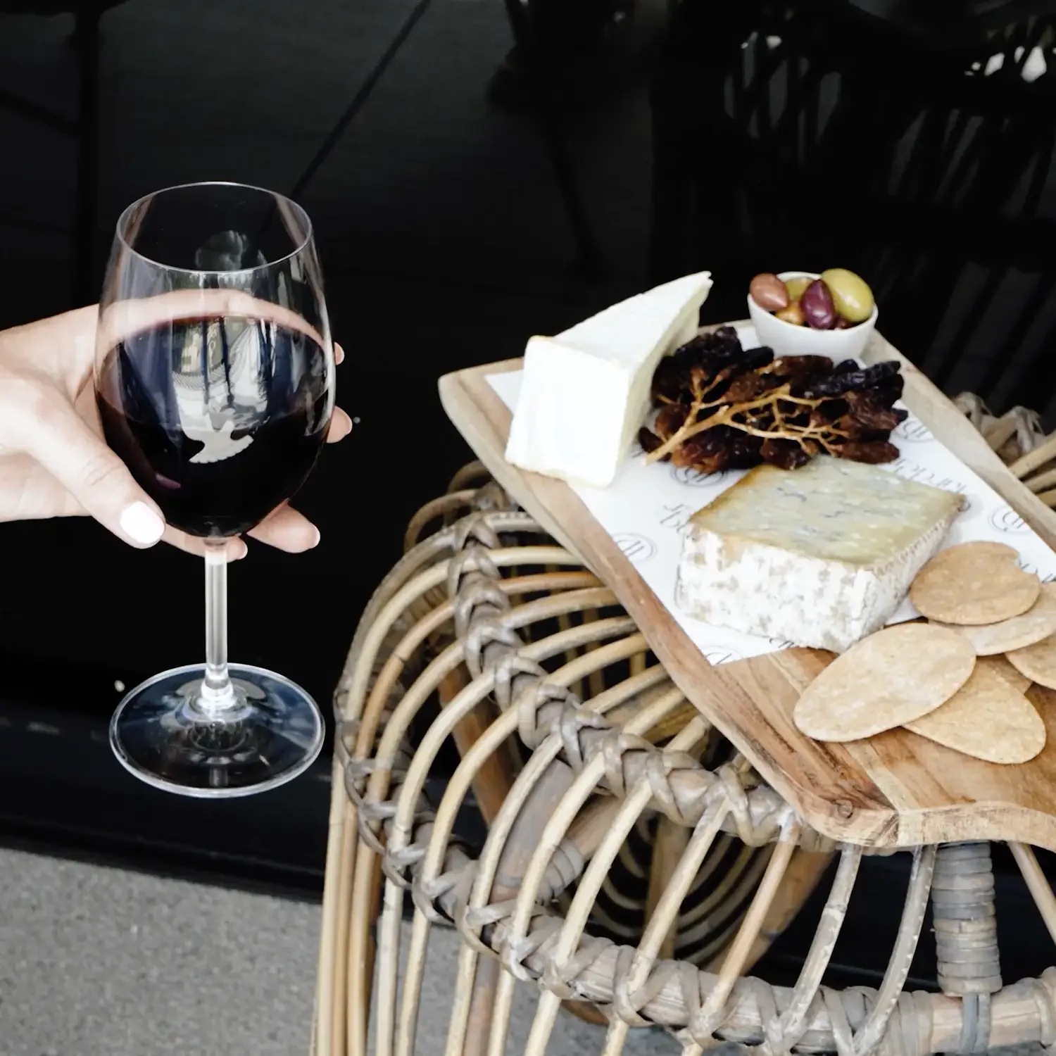 hand holding a wine glass next to a cheese board