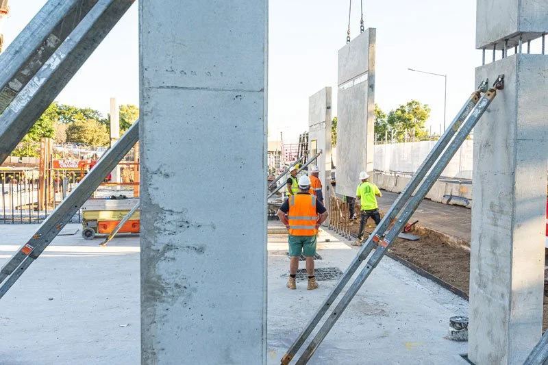 Construction workers in safety gear working on a concrete building site with large columns and steel supports.