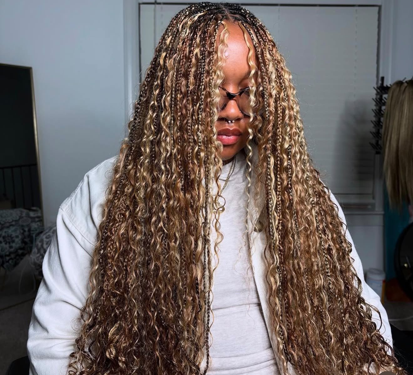 Personne portant de très longues tresses ondulées brunes et blondes, avec un pull blanc.