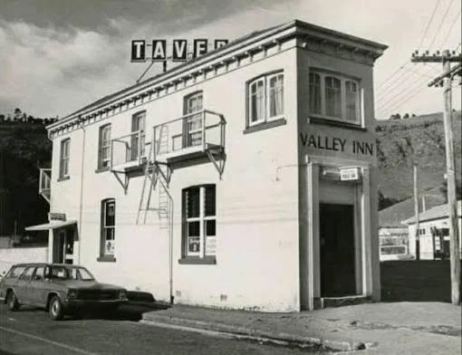 Historic black-and-white photo of the Valley Inn tavern in a two-story corner building, with a vintage car parked outside.