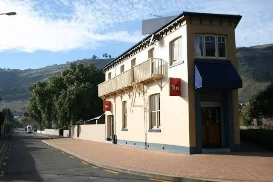 Historic cream-colored two-story building with balconies and red signs on a mountain-lined street