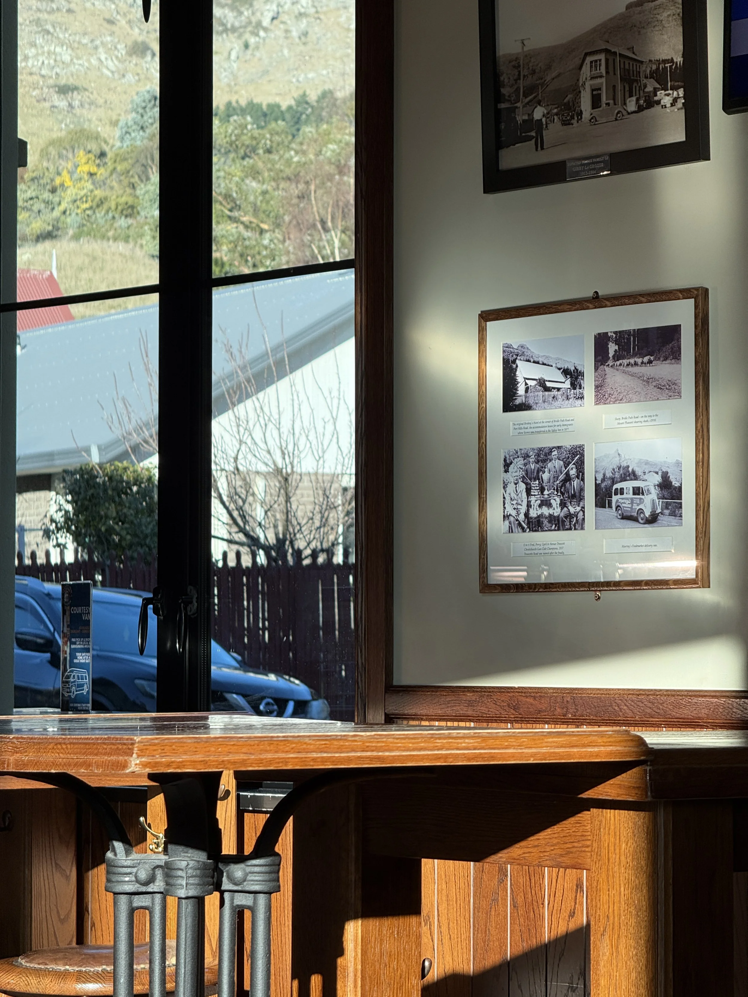 Museum interior with framed historical photographs, mountain scenery visible through windows, and a wooden counter with stools.