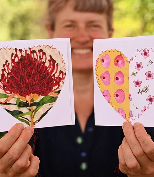 Katy Hood smiling person holding two colorful hand-embroidered heart cards with native Australian floral designs