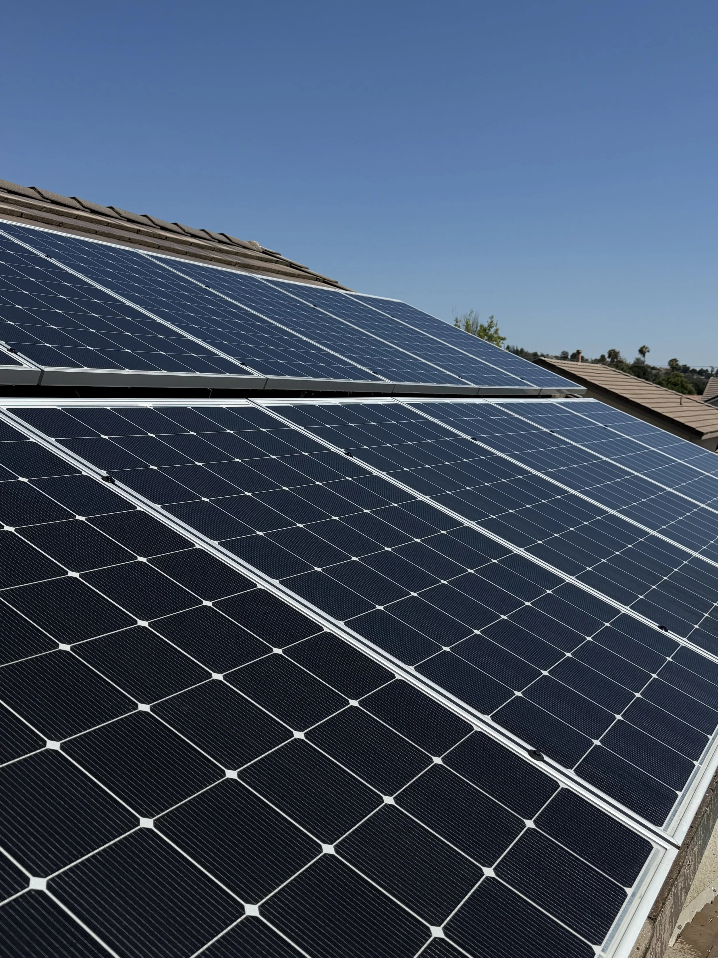 Multiple large solar panels installed on a roof under a clear blue sky.
