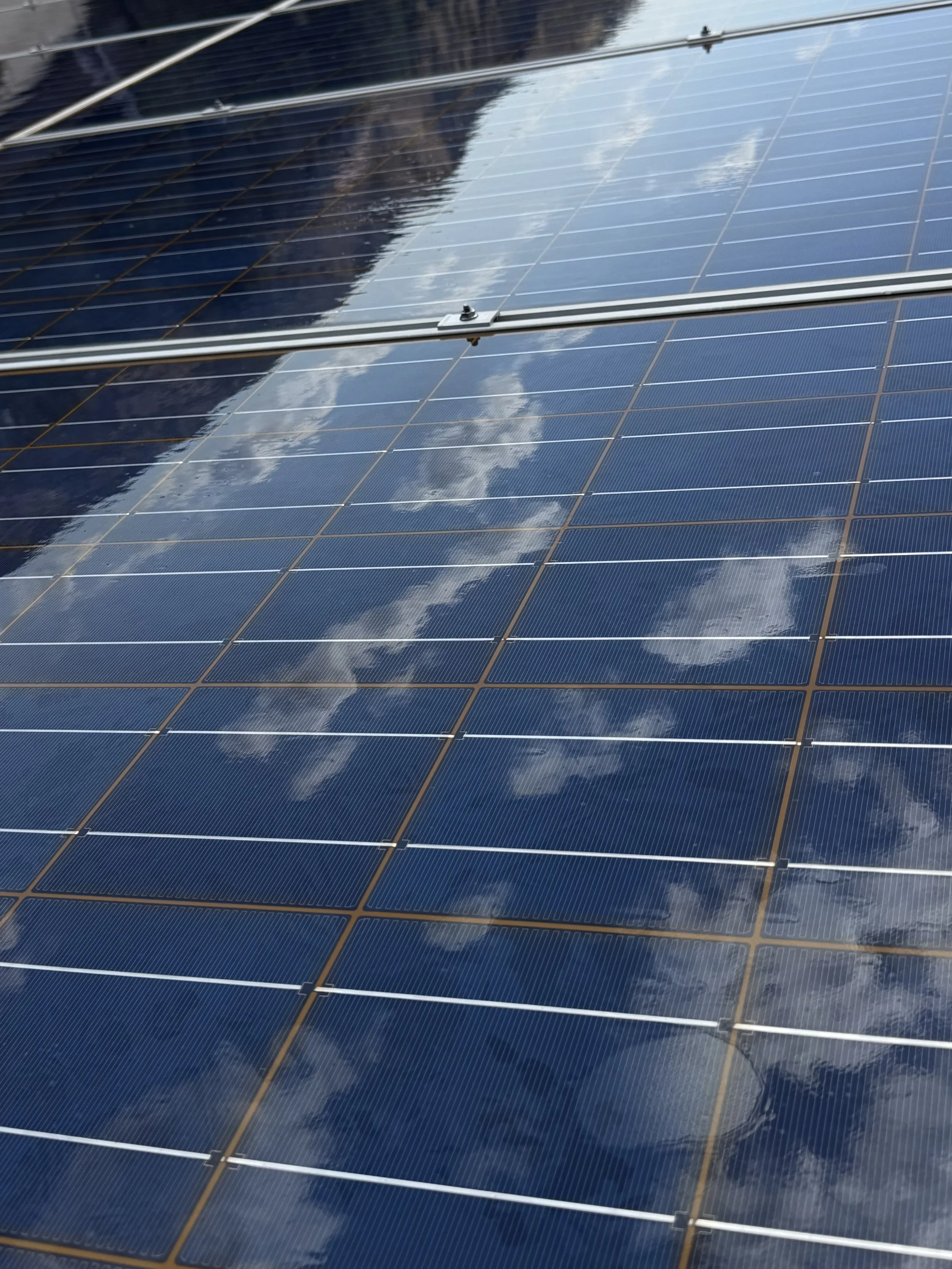Close-up of solar panels reflecting blue sky and clouds.