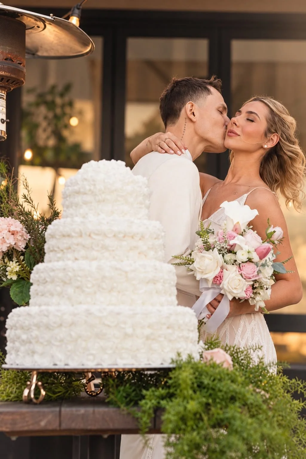 Couple kissing behind a white rose wedding cake and pink florals at a styled celebration, Gold Coast