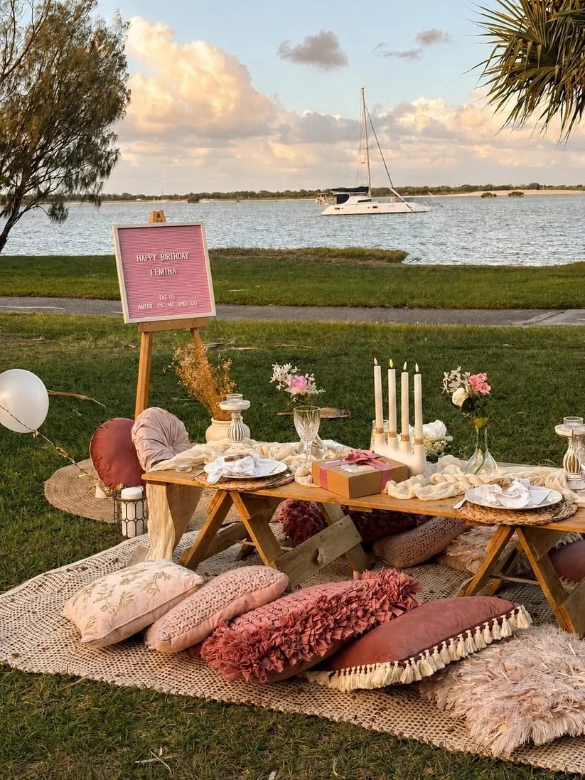 Pink birthday picnic setup by the water with a sailboat behind, Gold Coast