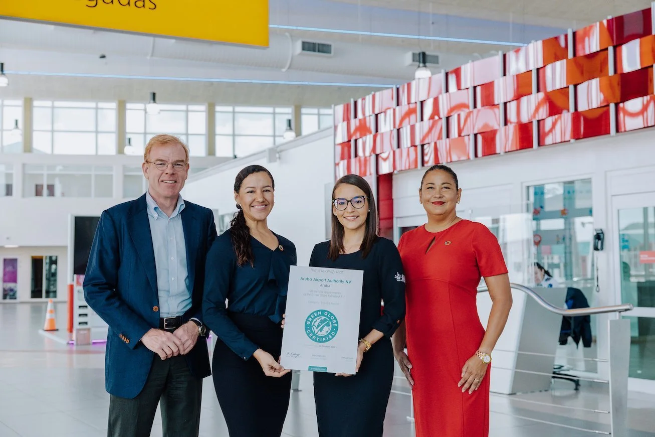 Four professionals standing inside an airport terminal, holding a green-globe-certified sign, smiling for the camera.