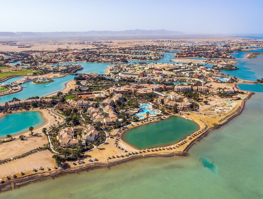 Aerial view of a resort with multiple swimming pools, sandy beaches, palm trees, and water bodies set in a desert landscape.