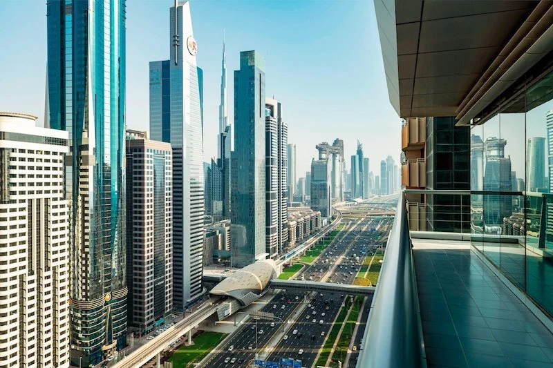 View from a modern high-rise balcony overlooking a futuristic cityscape with tall glass skyscrapers and busy highways.