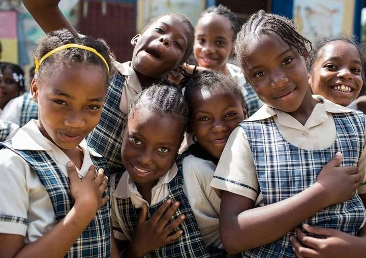 Group of young girls in school uniforms smiling and posing for the camera outside.