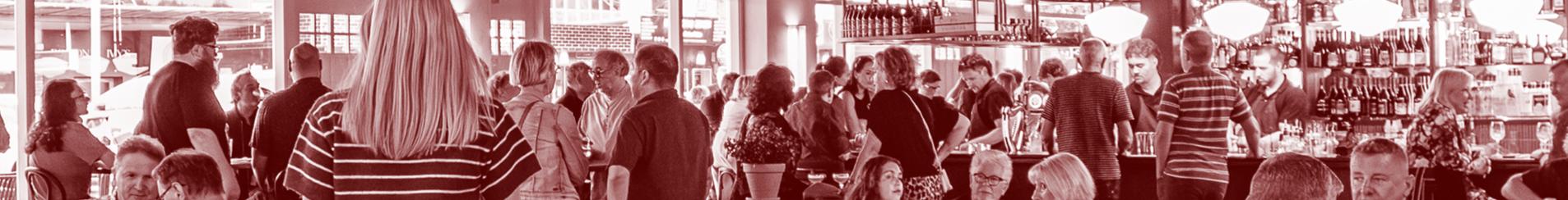 Interior of a busy café or restaurant with many people standing and sitting, chatting, and ordering at the bar.