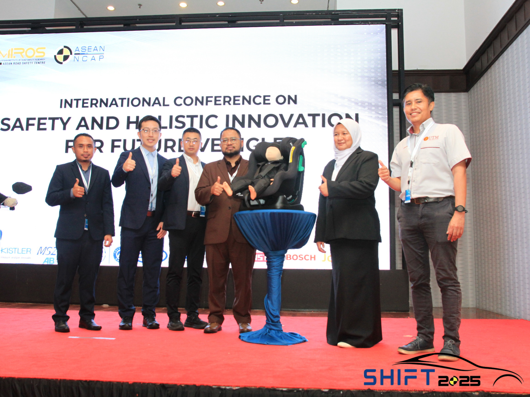 Representatives posing alongside the ASEAN CPD-DS3 Child Presence Detection Dummy displayed in a child restraint system during its product launch at the International Conference on Safety and Holistic Innovation for Future Technologies (SHIFT 2025).