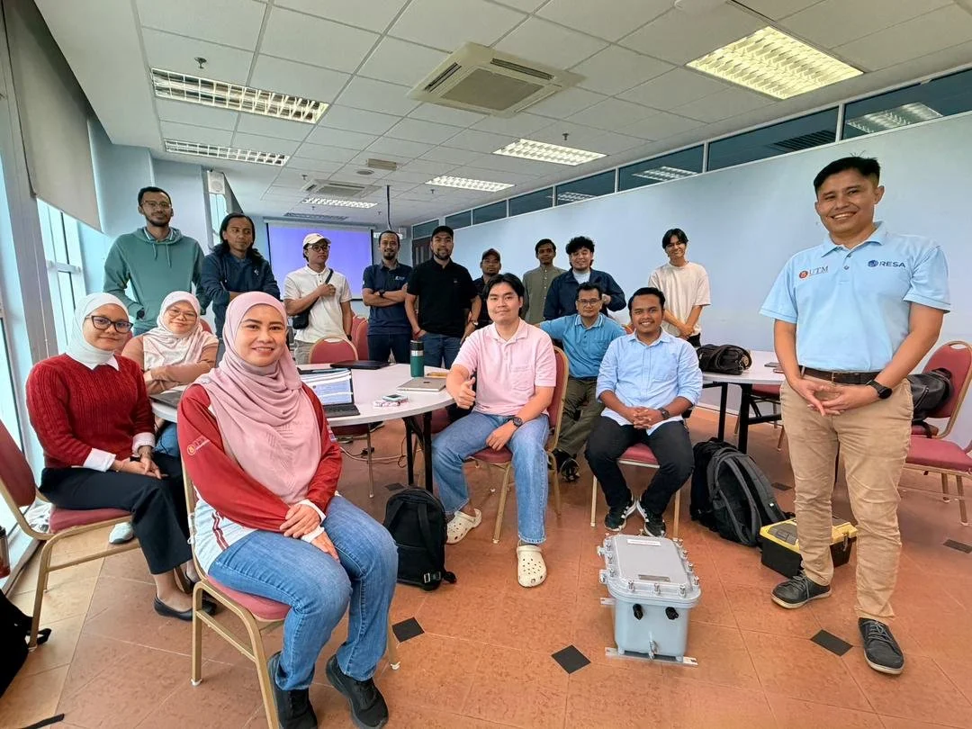 Group photo of ACTS, TNF Group, INVICOM representatives, and UTM students during a Structural Dynamic Monitoring (SDM) technical training session, featuring monitoring equipment in a classroom setting.