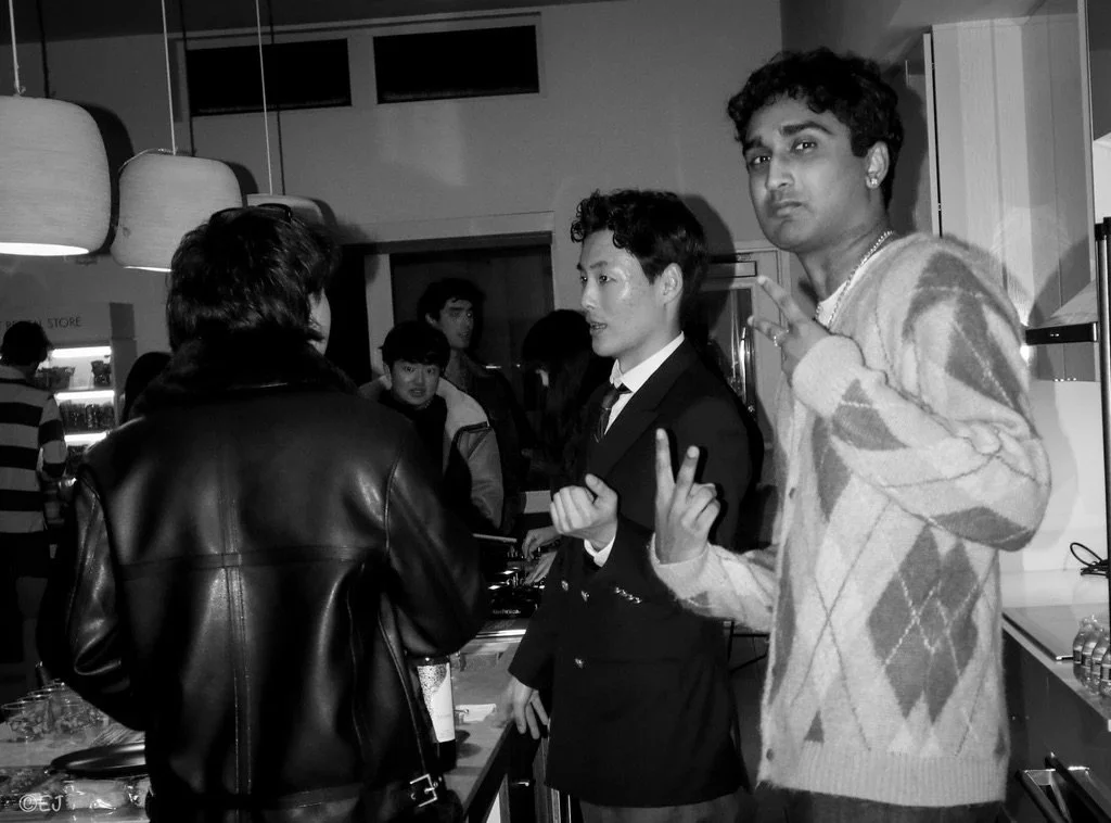 A group of young people at a social gathering or party in an indoor setting, with some individuals engaged in conversation and others posing for the photo.