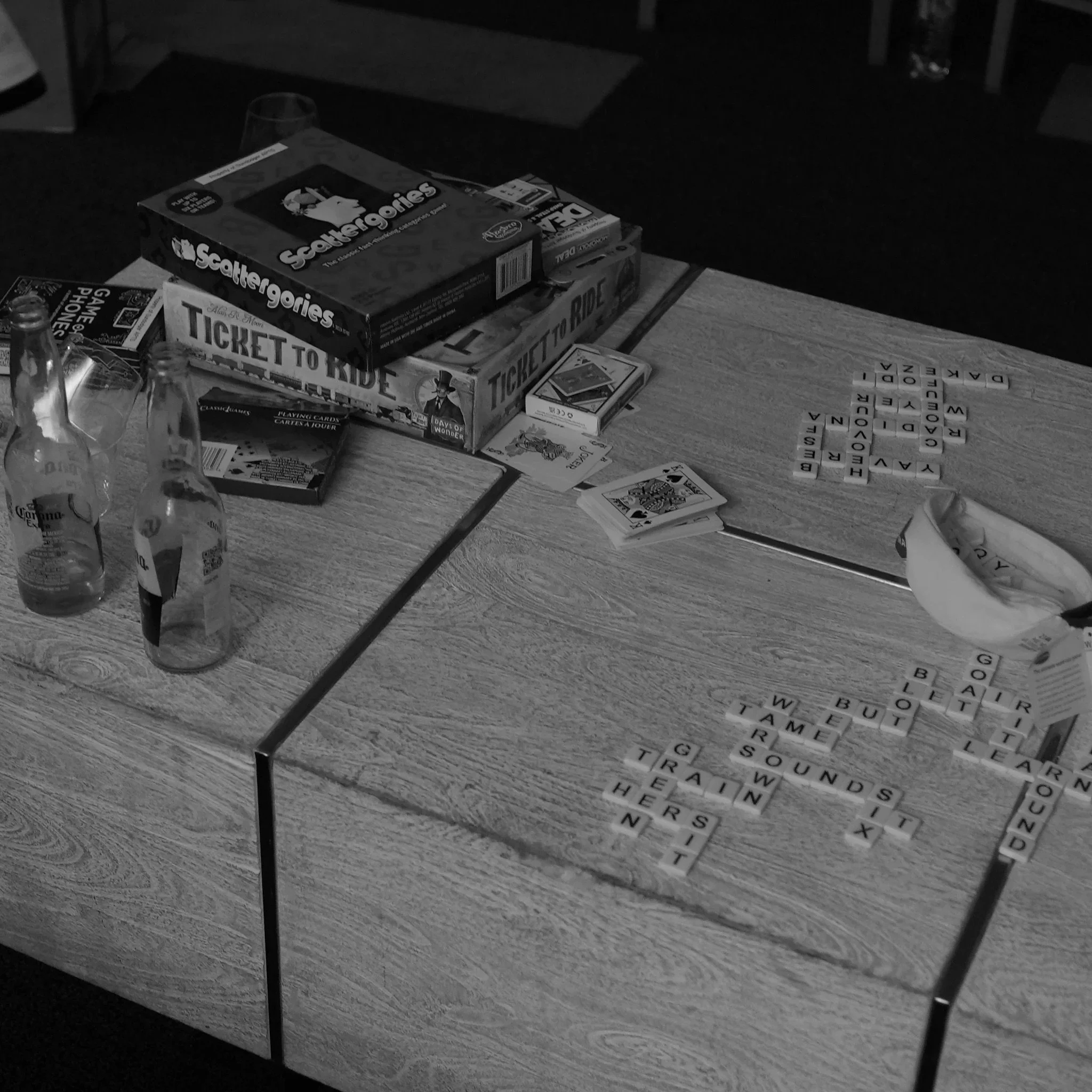 Table with board games, Scrabble tiles, and playing cards, along with bottles and a glass.