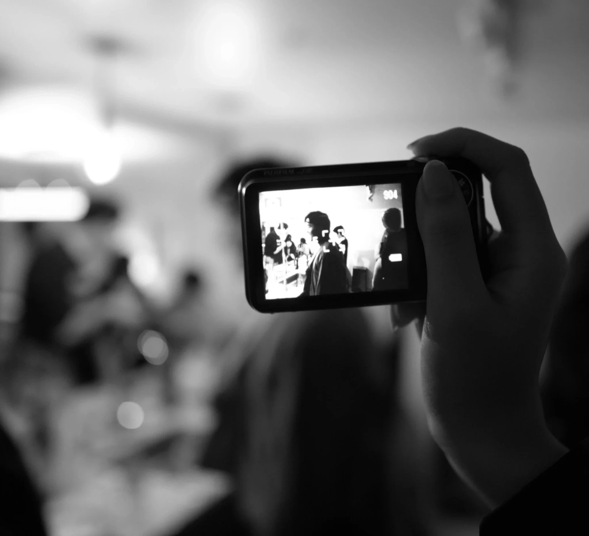 A person taking a photo of a group of people on a smartphone camera in a black-and-white image.