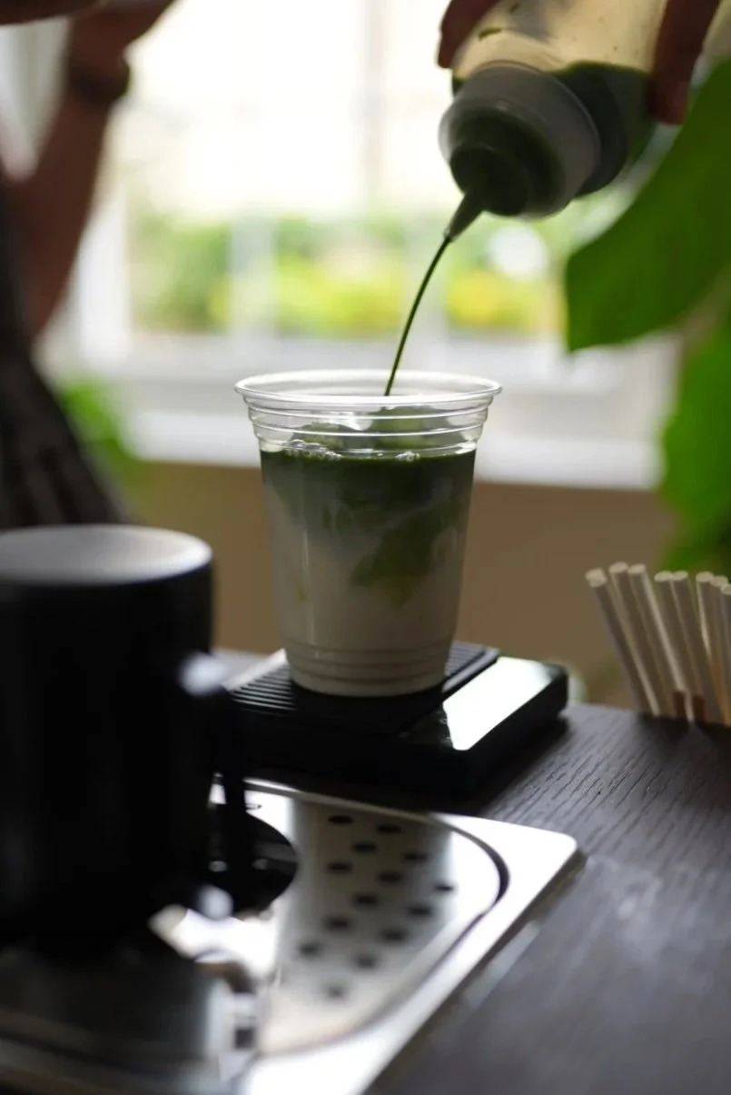 Green matcha being poured into a clear cup on a digital scale
