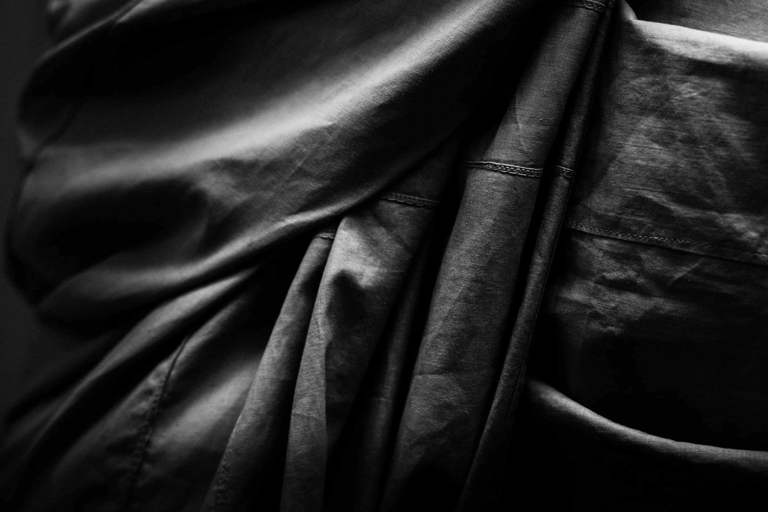 Close-up of black fabric with visible stitching and folds, taken in a dark setting.