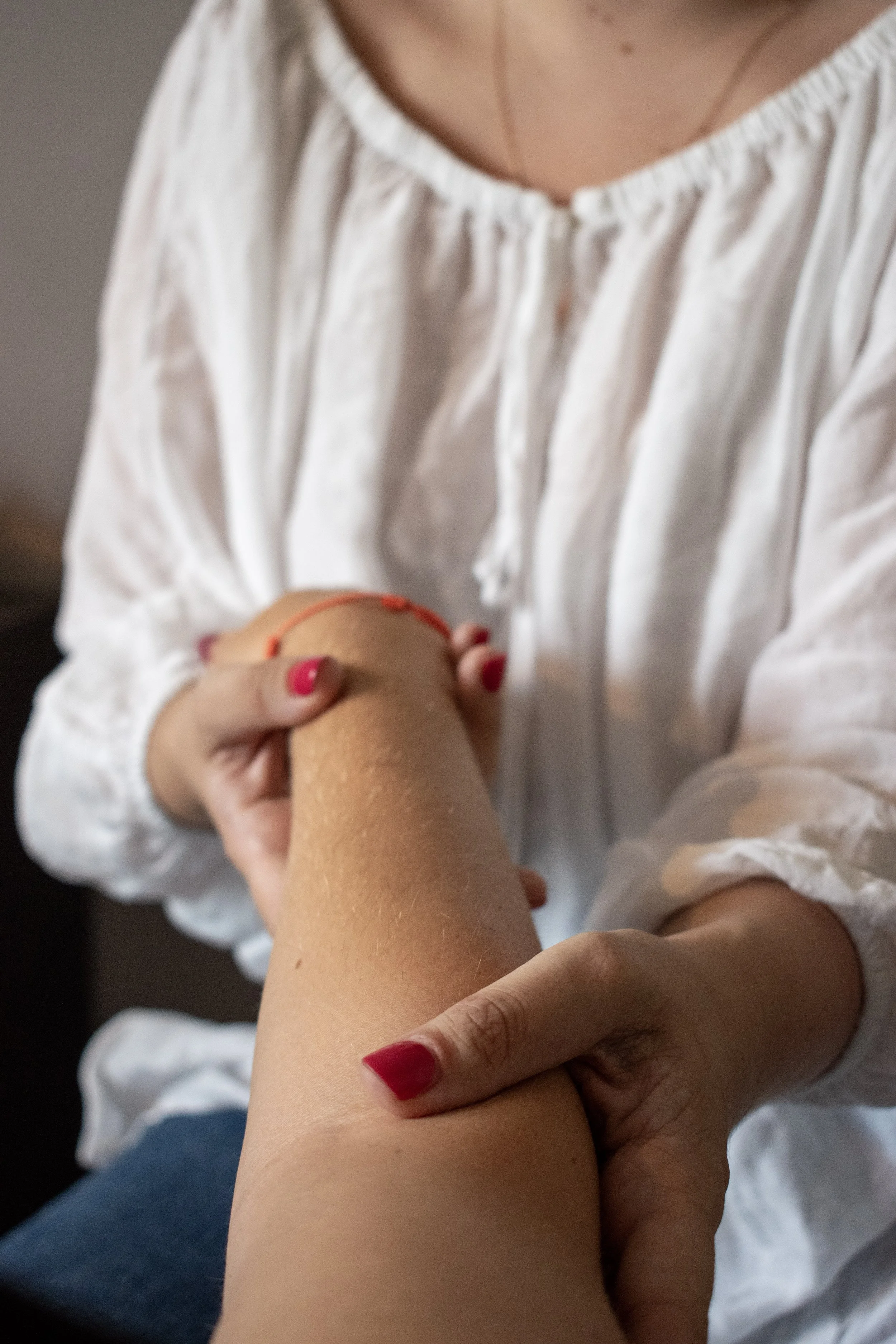 Gros plan sur une femme aux ongles rouges massant le genou d’une personne âgée.