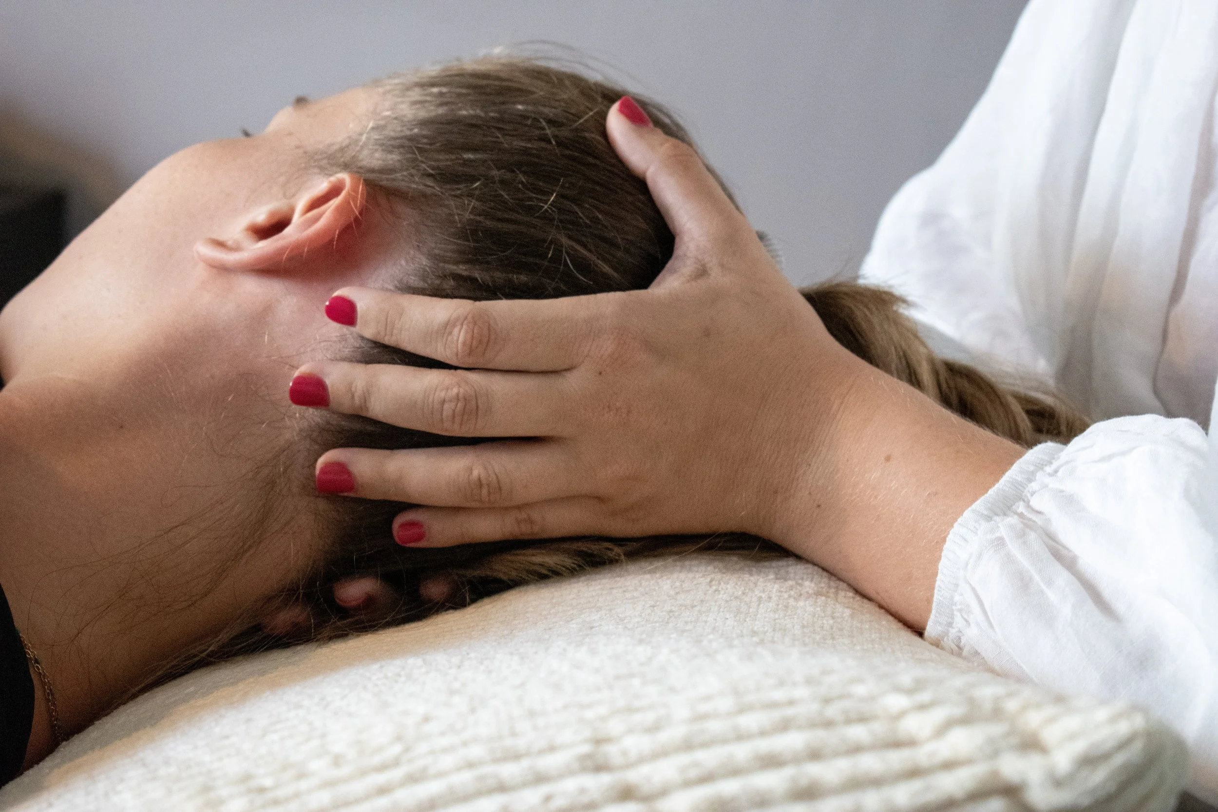 Femme allongée recevant un massage de la tête et du cou par une praticienne.