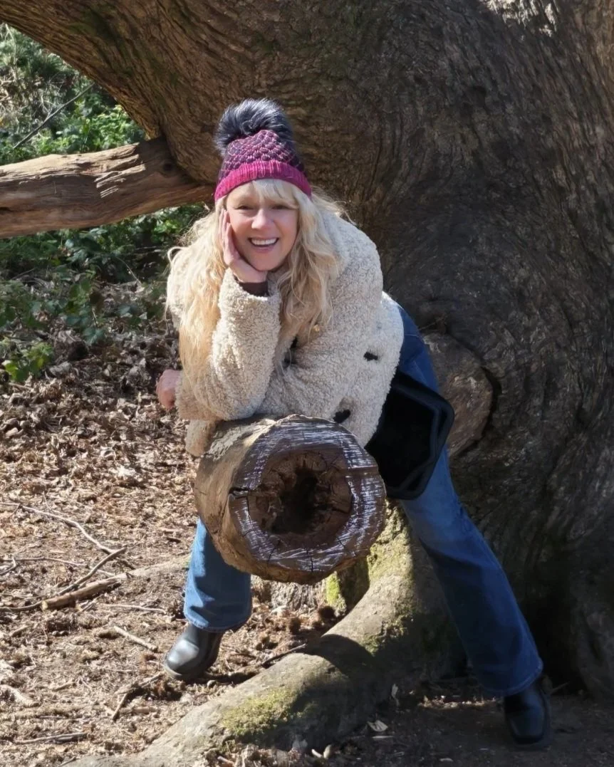 Smiling woman in a pink knit hat posing beside a massive tree trunk outdoors