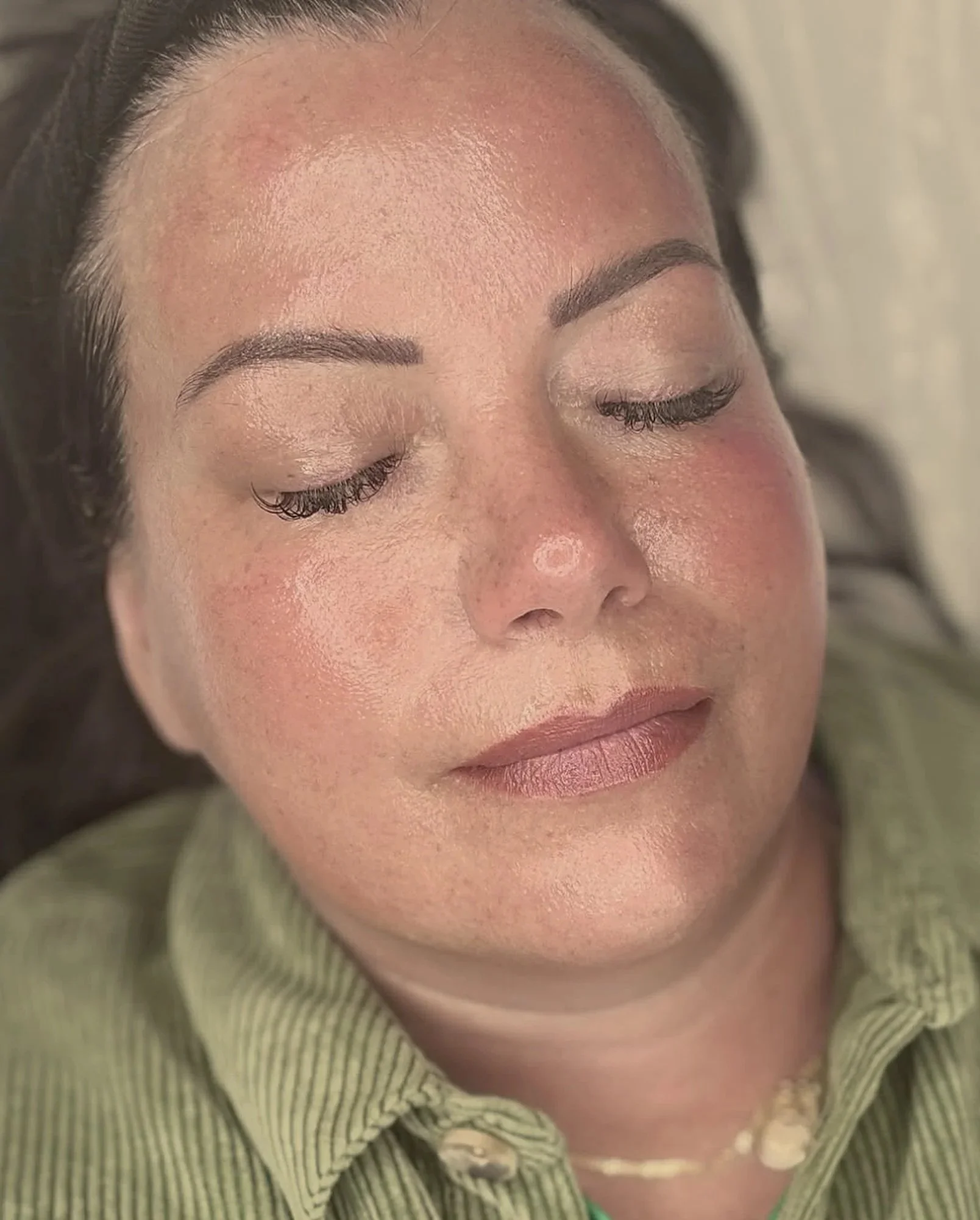 Close-up of a woman's face with closed eyes, showing her eyebrows, eyelashes, and skin texture, wearing a green and white striped shirt.
