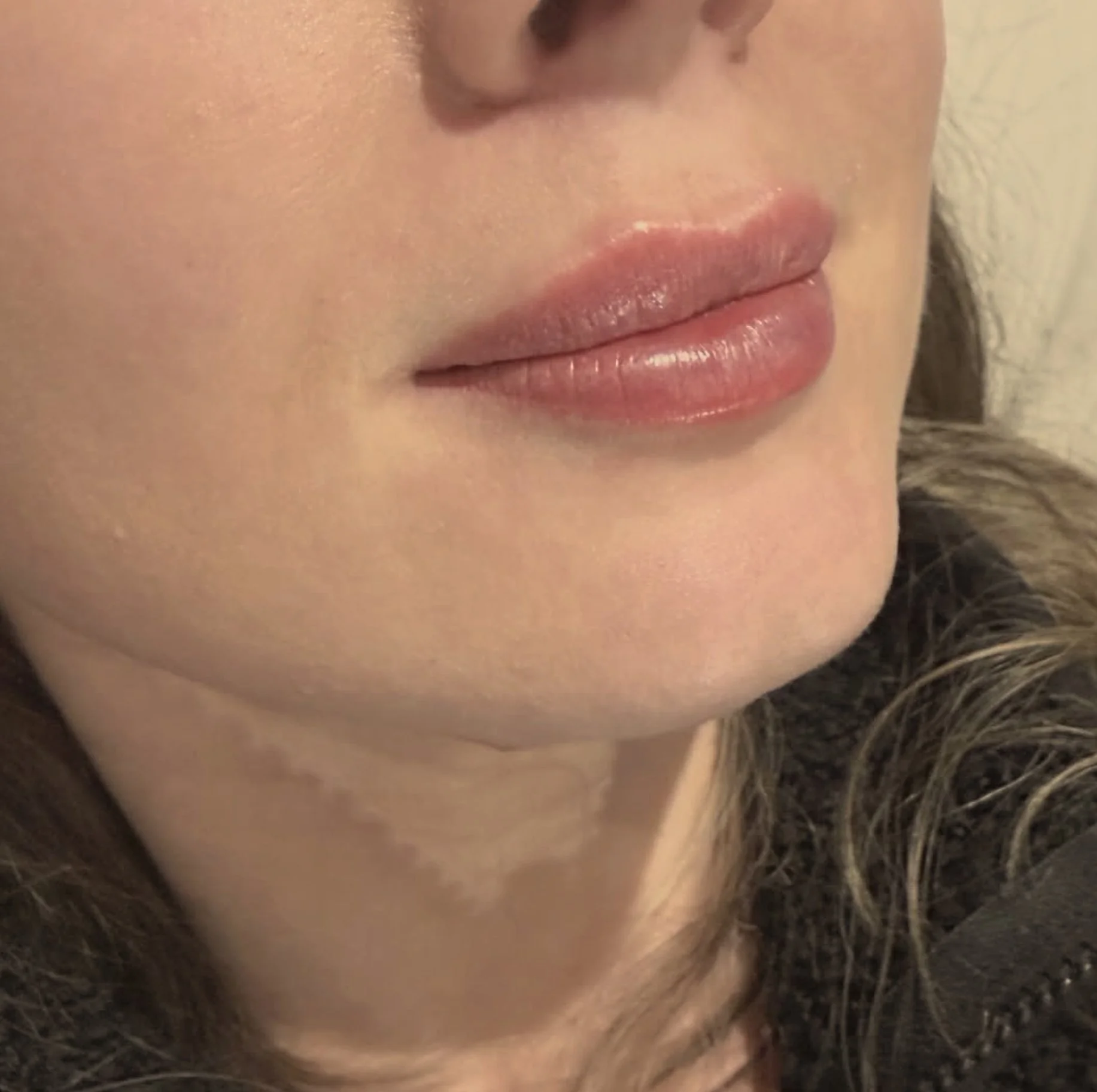 Close-up of a woman's lips with light makeup and slightly curled hair visible on the side.