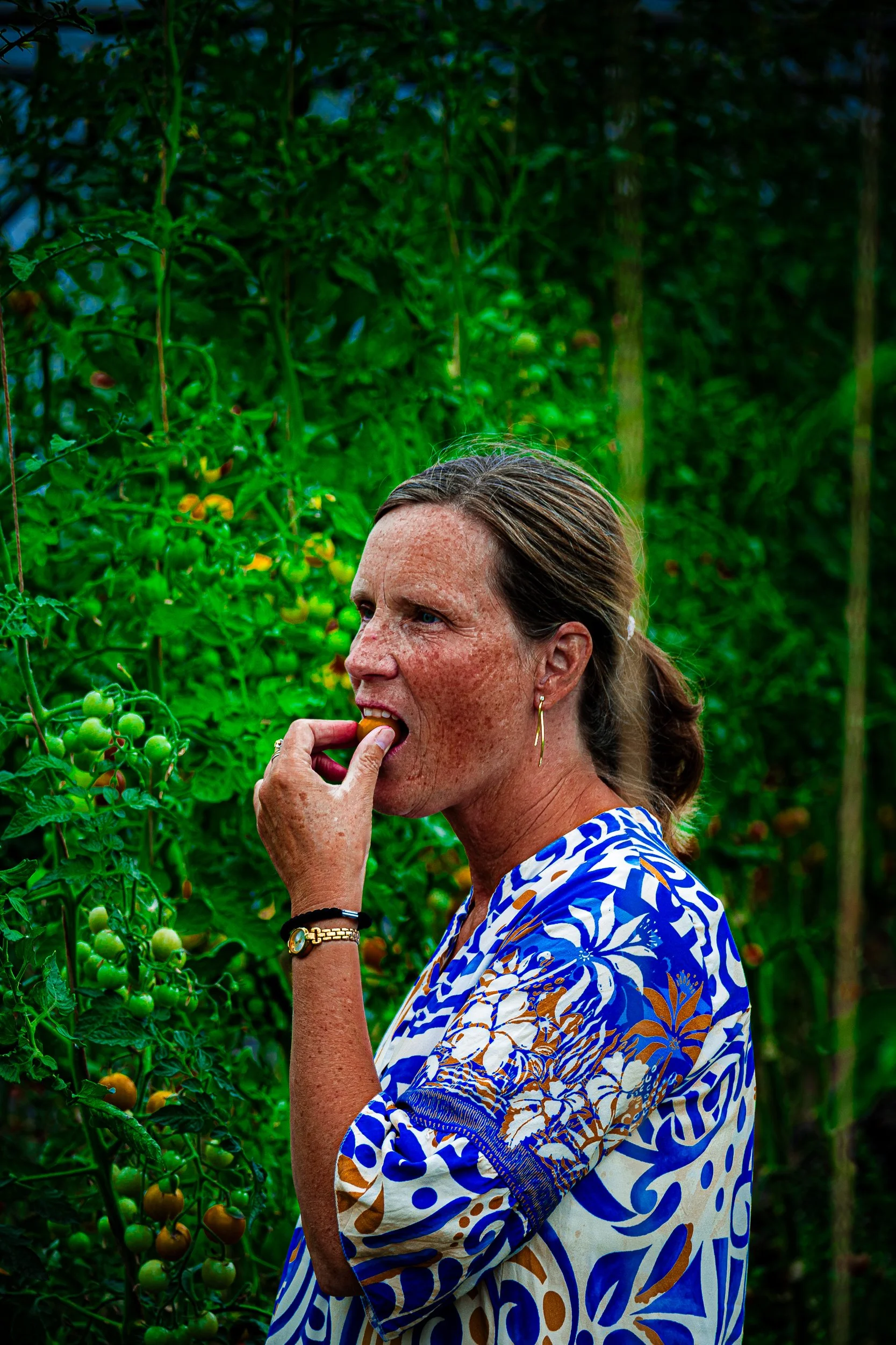Woman eating a small tomato in a lush garden