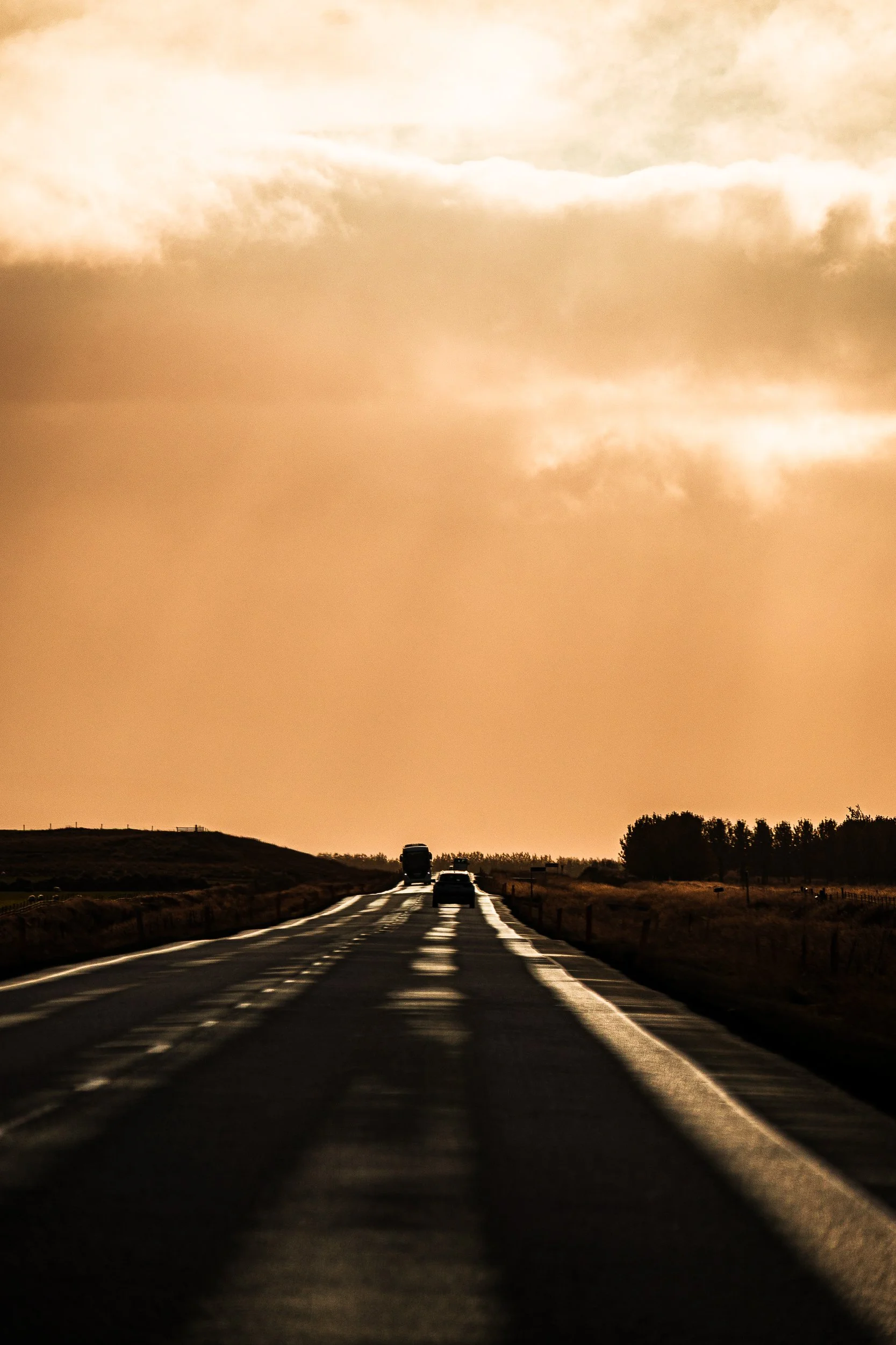 Cars traveling along a rural road beneath dramatic golden sunset clouds
