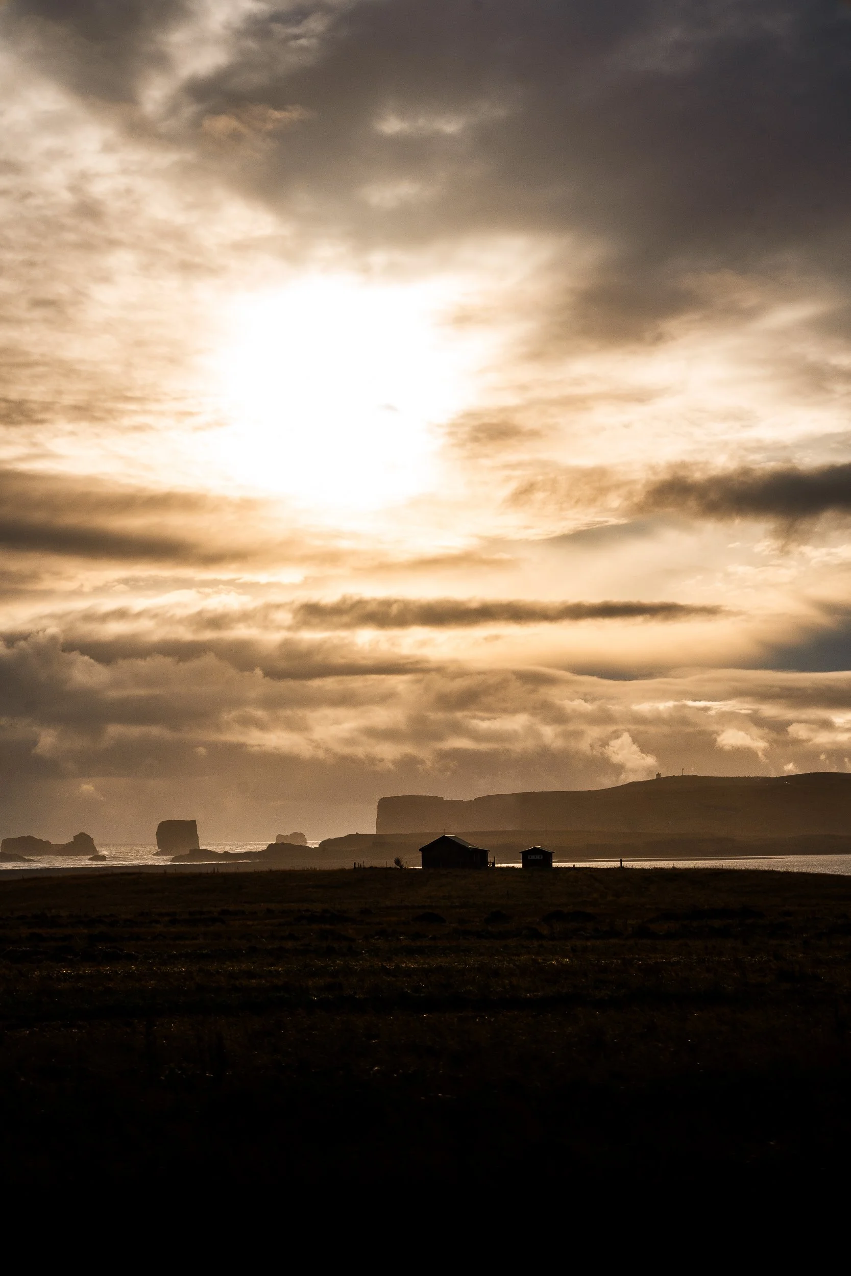 Dramatic sunset over a rugged coastline with sea stacks, cliffs, ocean, and silhouetted coastal cottages.