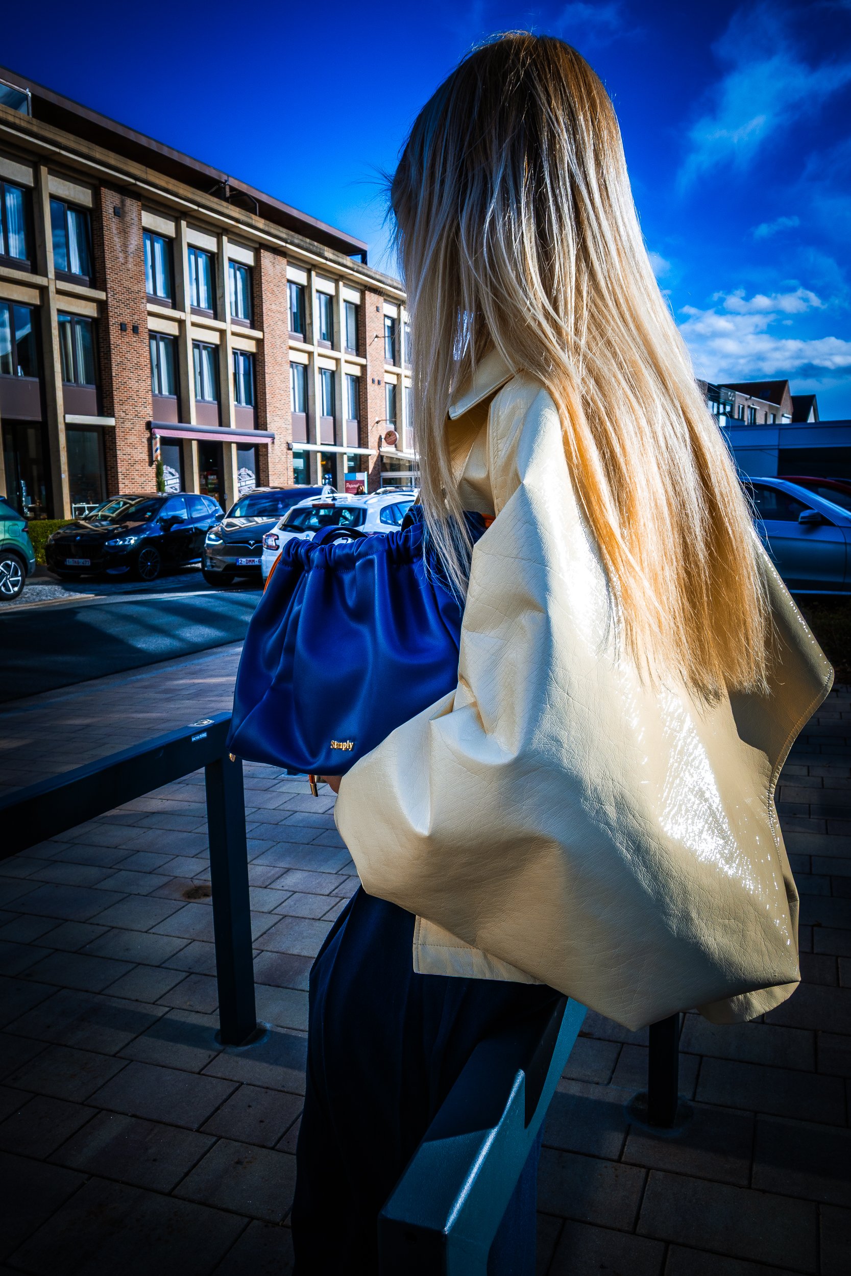 Woman with long blonde hair wearing a white jacket and carrying a blue handbag on a city street