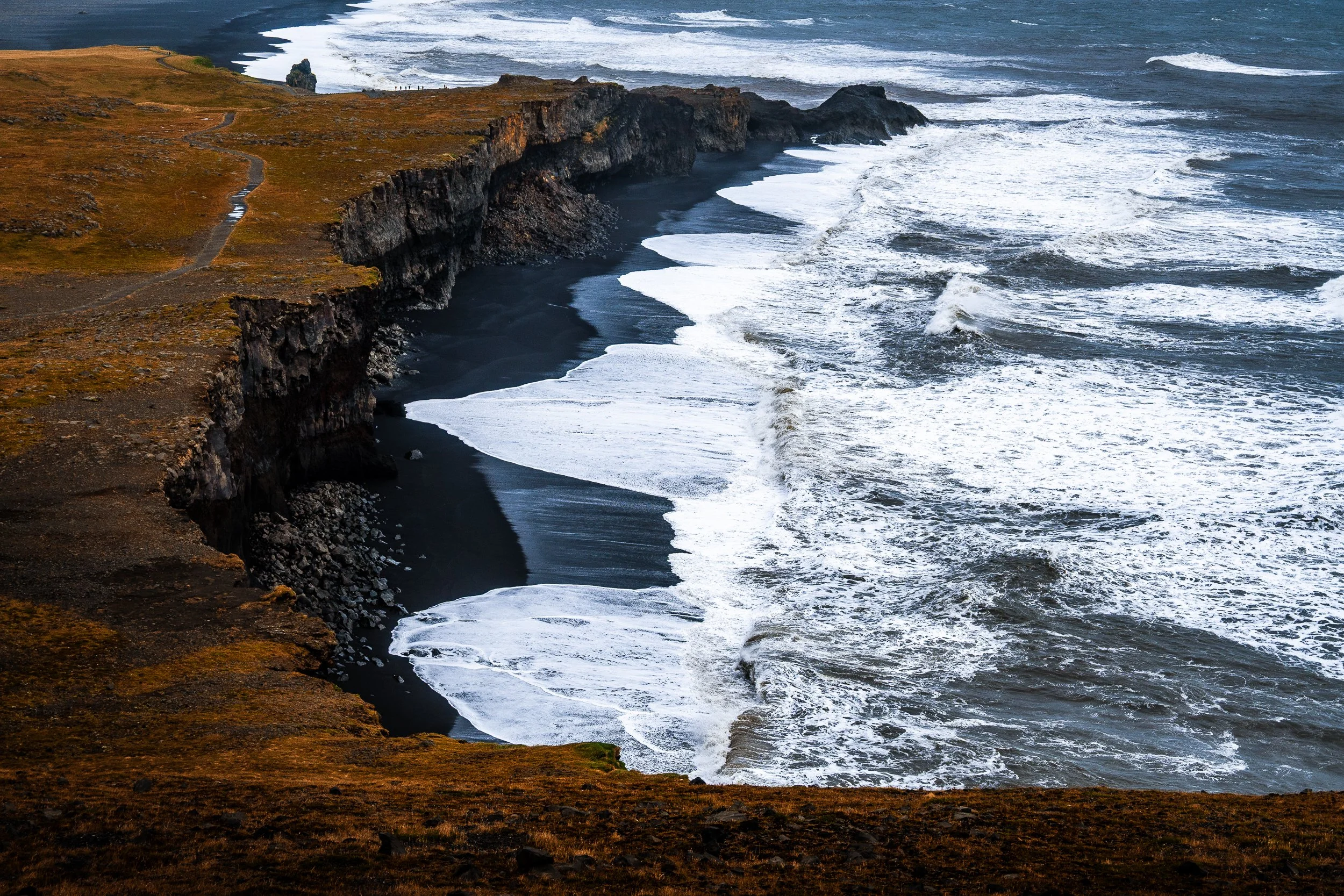 Dramatic Icelandic coastline with black sand beach, rugged basalt cliffs, and powerful ocean waves