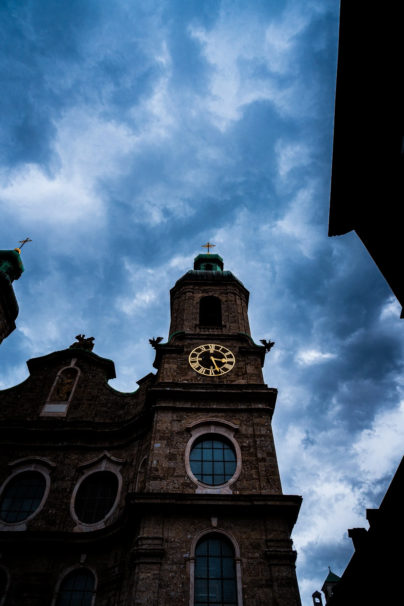 Low-angle view of a historic stone church facade with a clock tower, ornate statues, and cloudy blue sky