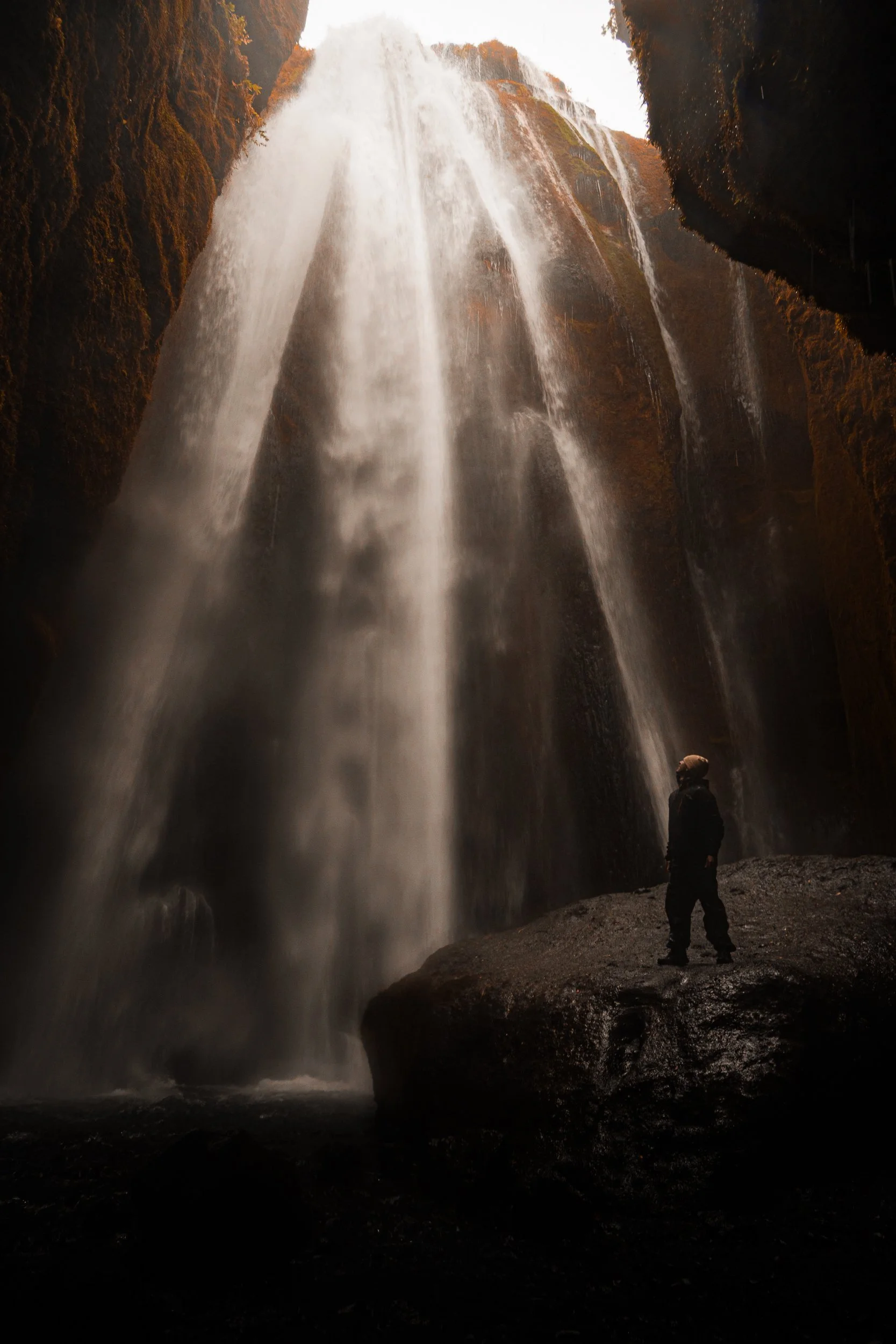 Hiker standing beside a towering waterfall cascading over a moss-covered cliff