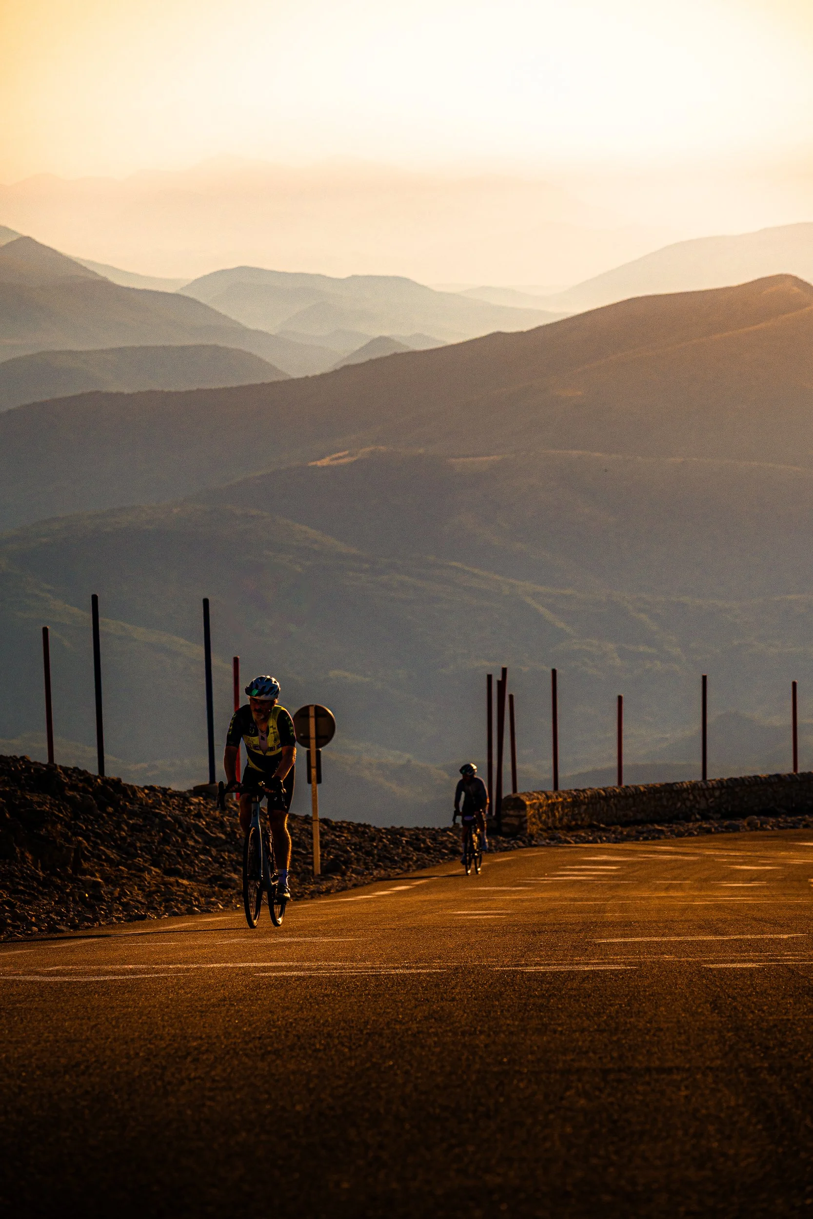 Cyclists climbing a mountain road at sunset with layered mountains in the background