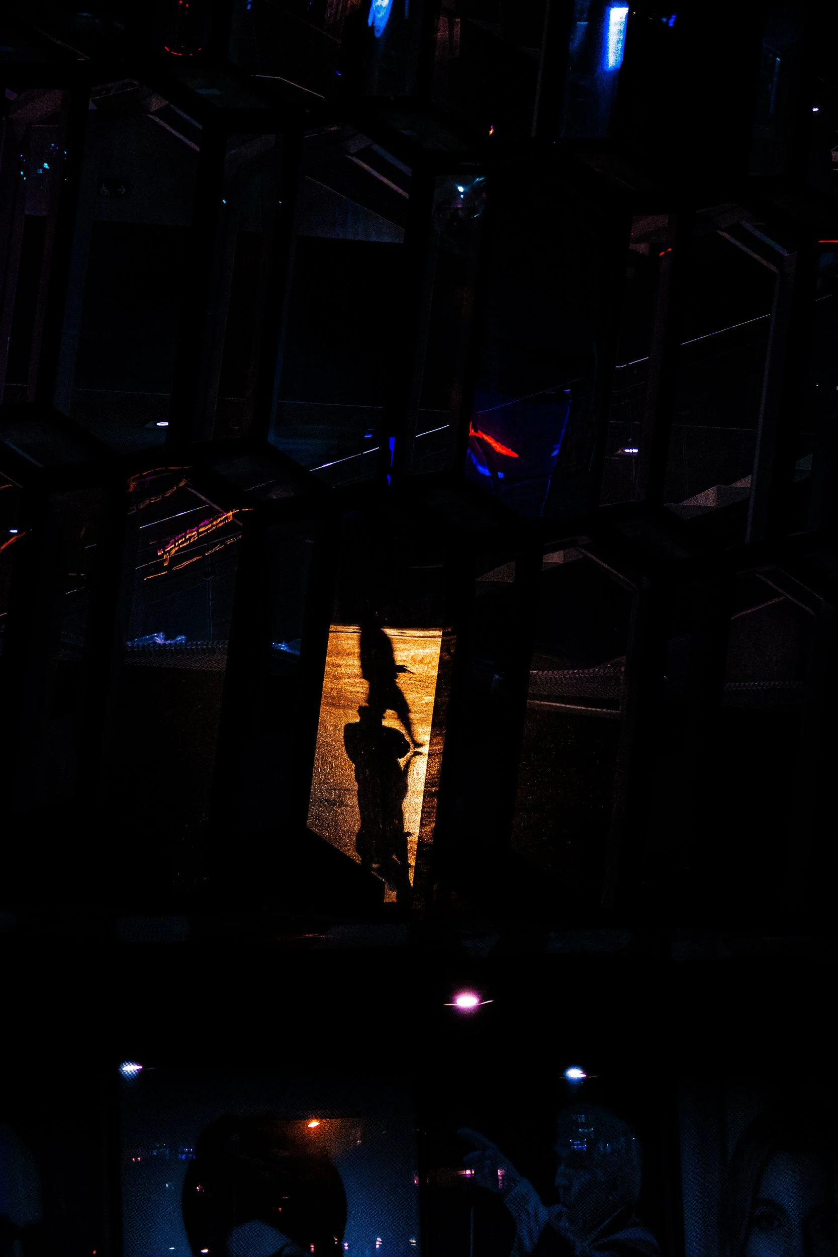 Dark indoor amusement attraction with silhouetted visitors, reflective surfaces, and colorful neon lighting.