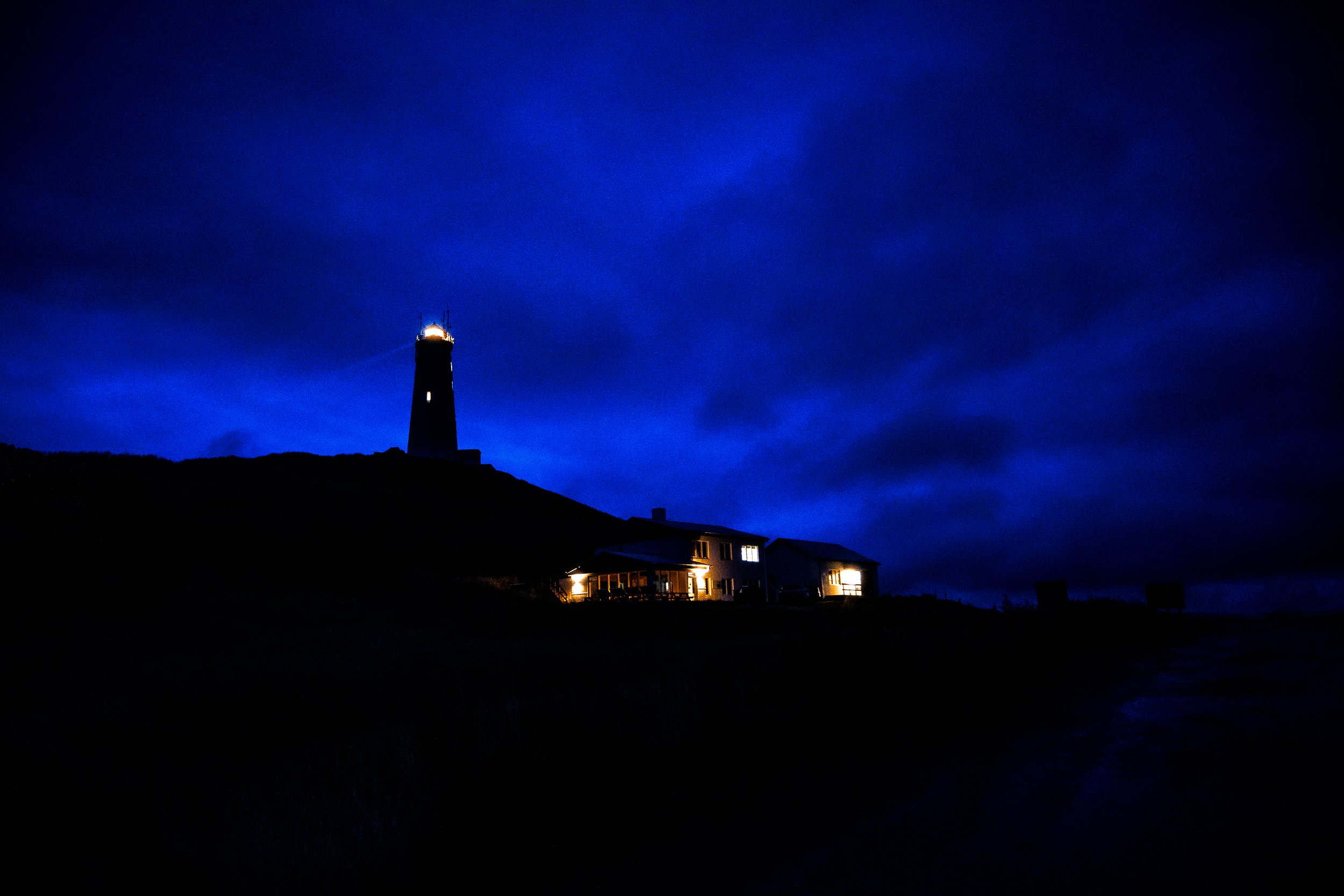 Lighthouse and illuminated coastal building silhouetted against a deep blue night sky