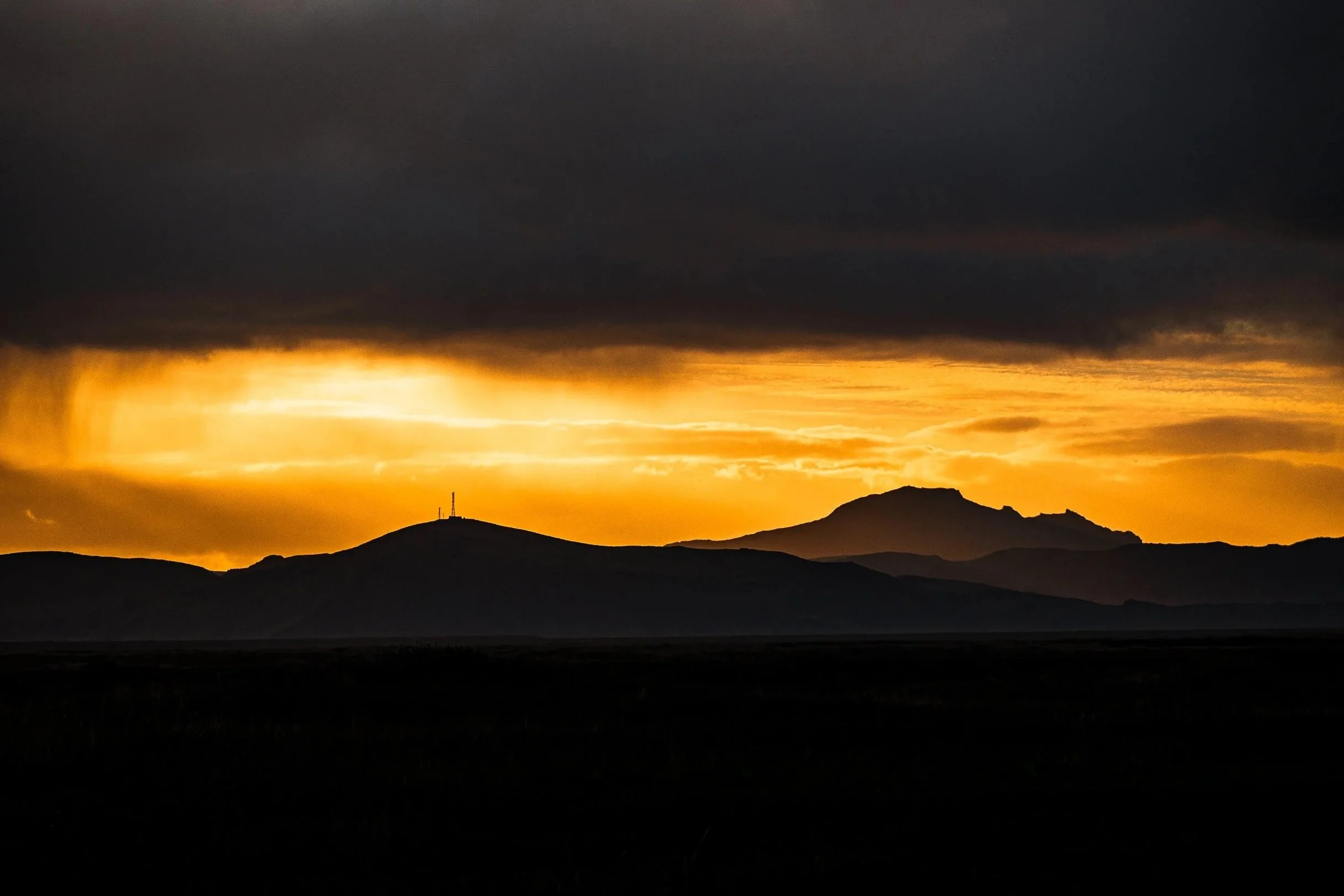 Silhouetted mountain range beneath dramatic dark clouds and a glowing orange sunset