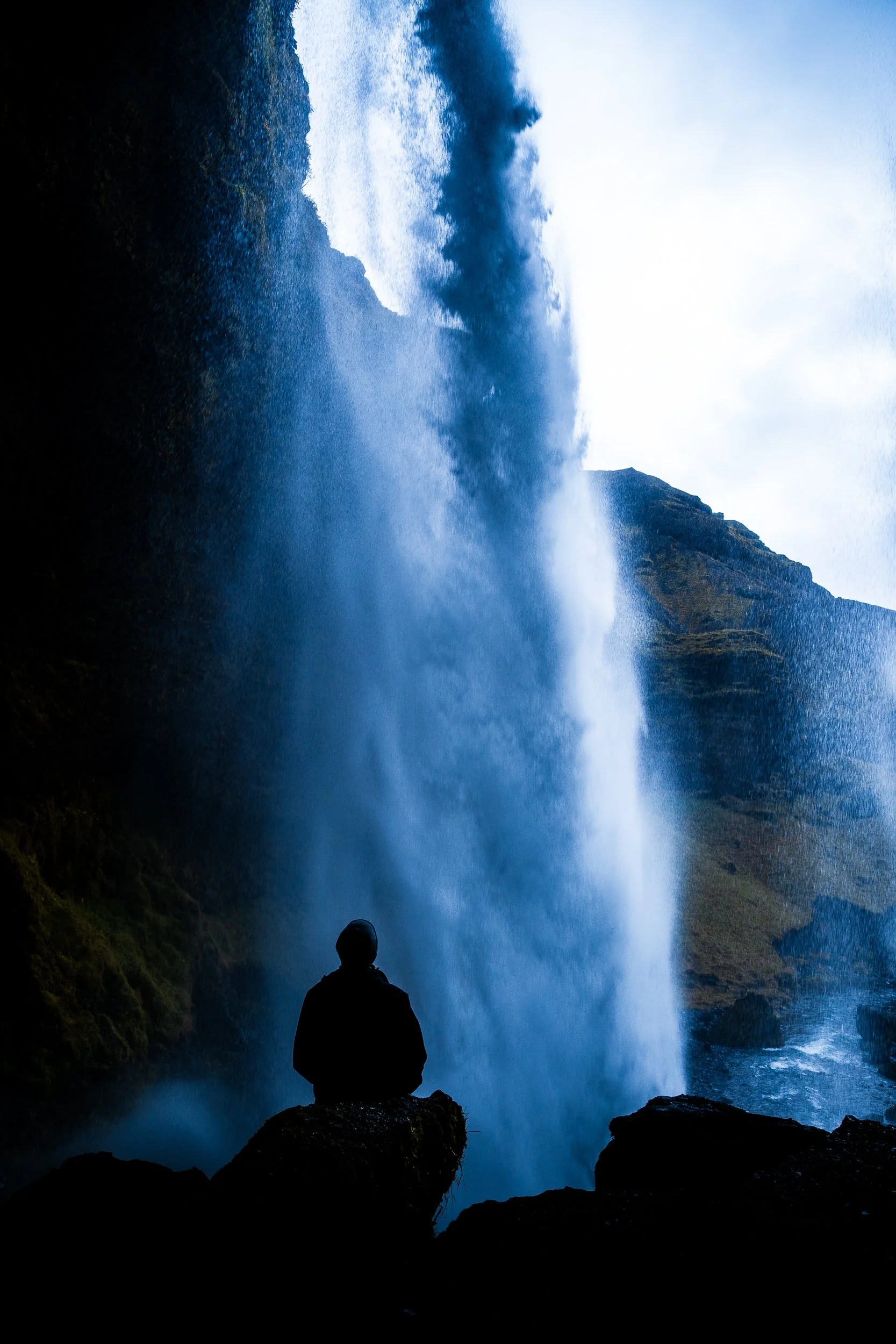 Silhouetted person viewing a powerful waterfall between rugged mountain cliffs