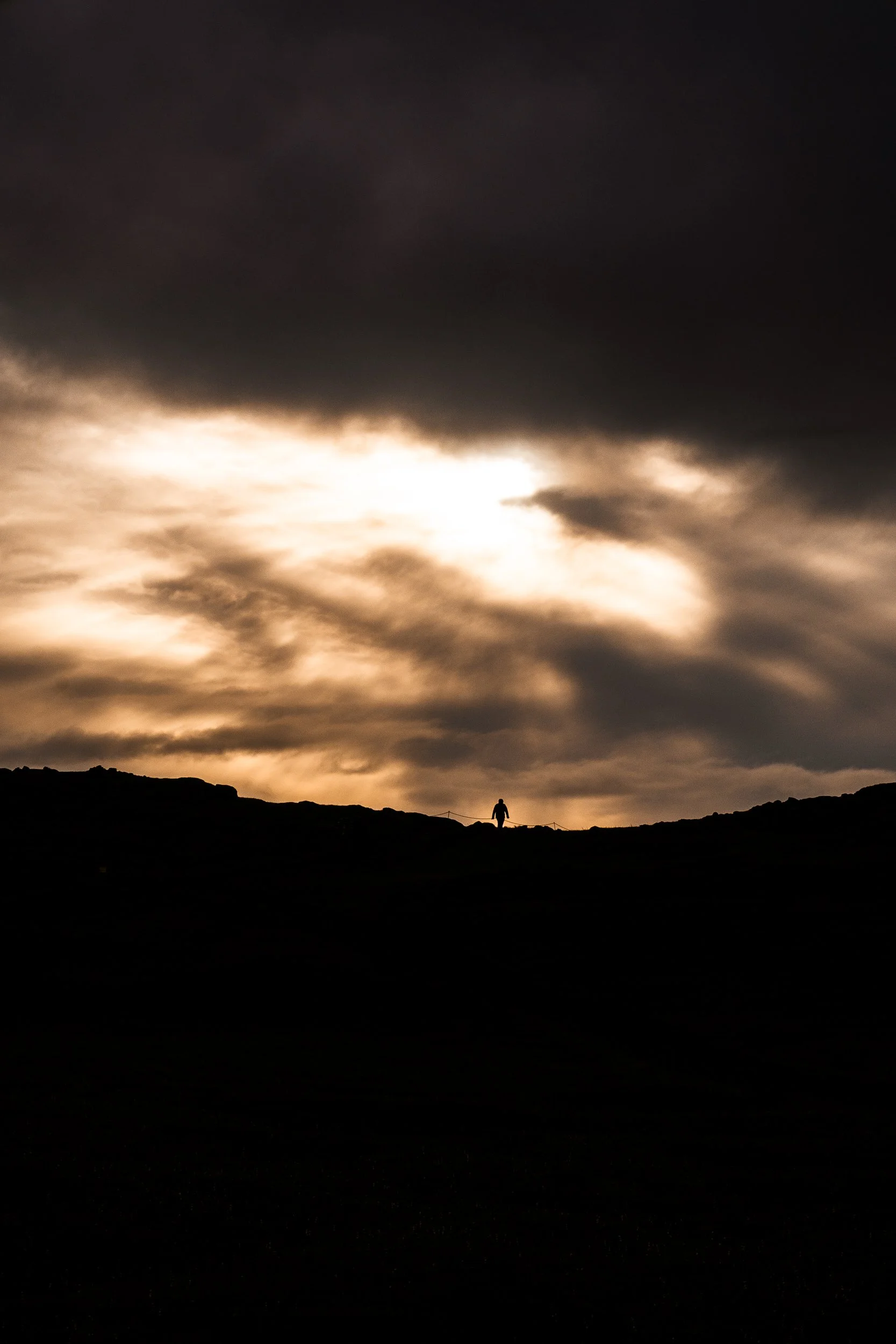 Silhouetted hiker on a rocky ridge beneath dramatic golden sunset clouds