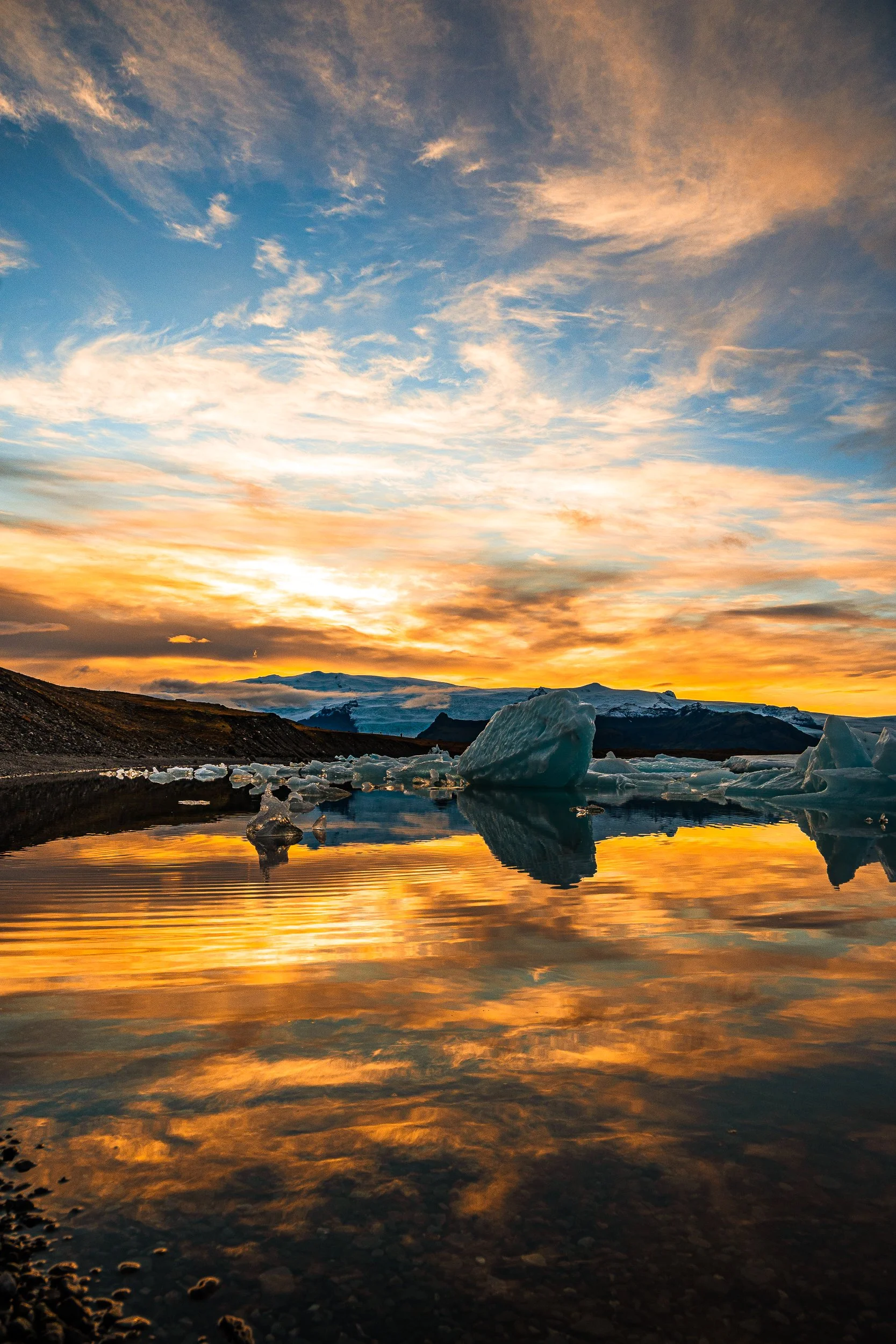 Sunset over an Icelandic glacial lagoon with floating icebergs, mountains, and golden reflections in the water