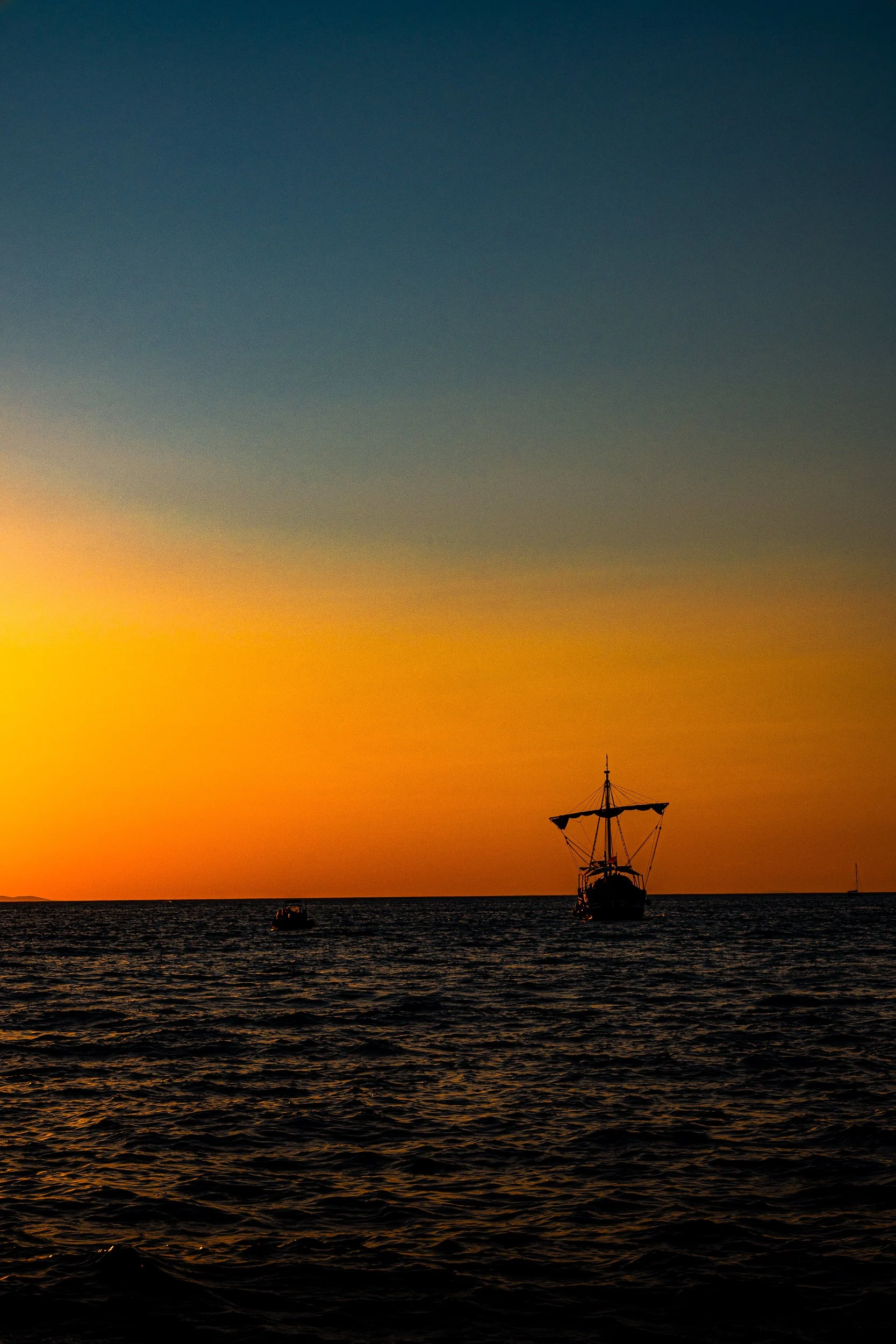 Silhouetted sailboat on dark ocean waters during a vivid orange sunset