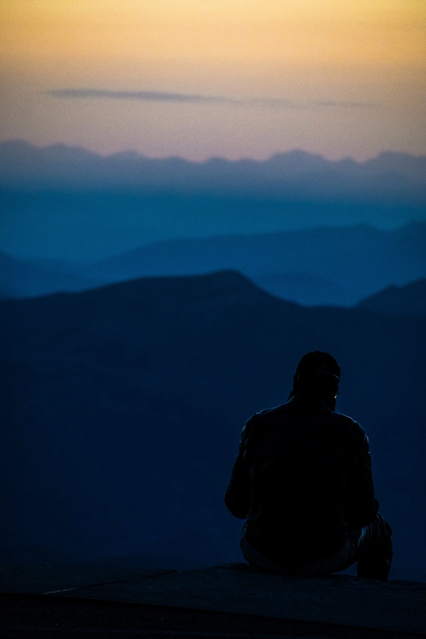 Silhouetted person sitting and looking over layered mountain ridges at dusk