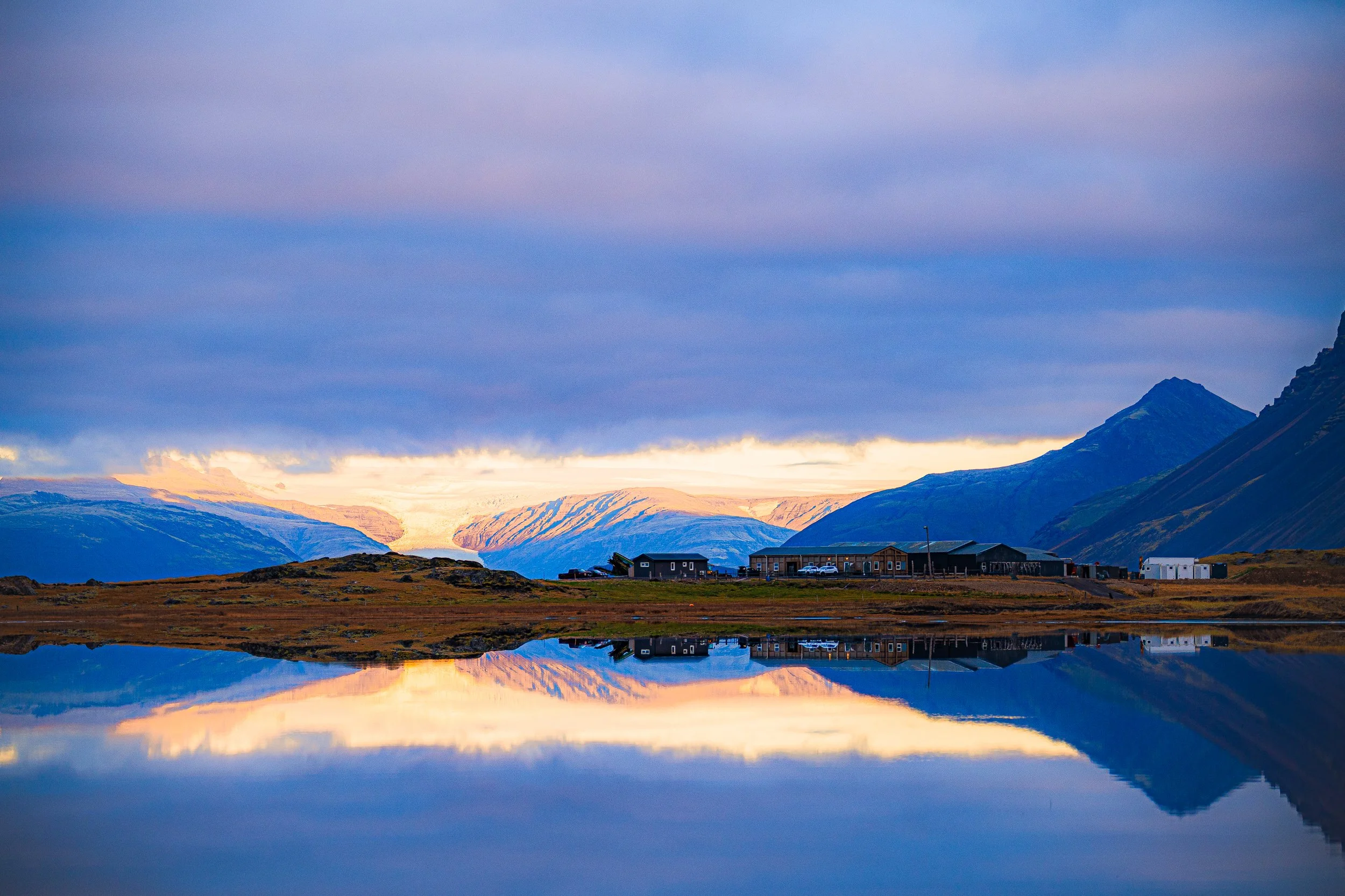 Mountain settlement reflected in a calm lake beneath a colorful sunset sky